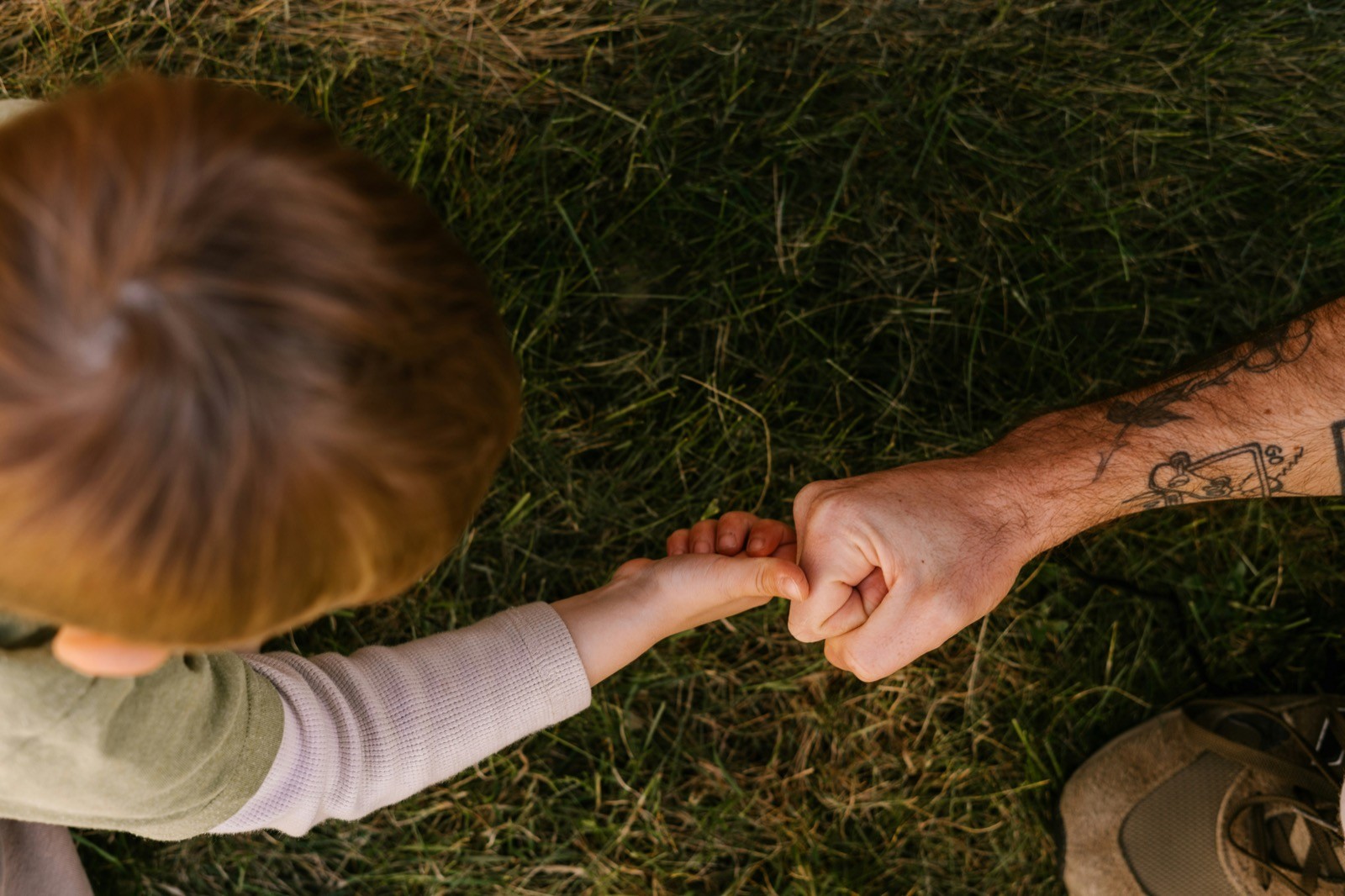 Young children and parent lying on a grass surface and smiling outside.