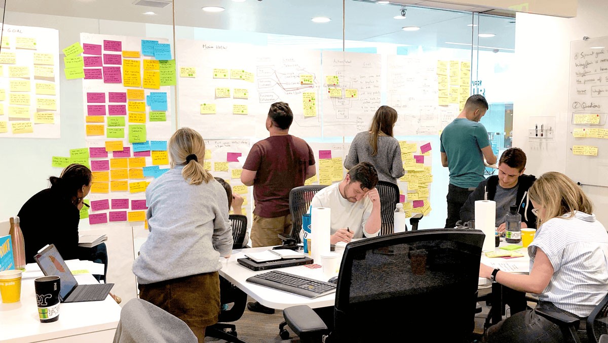 Wayfair workshop in progress with team members working at desks and reviewing sticky notes on glass walls