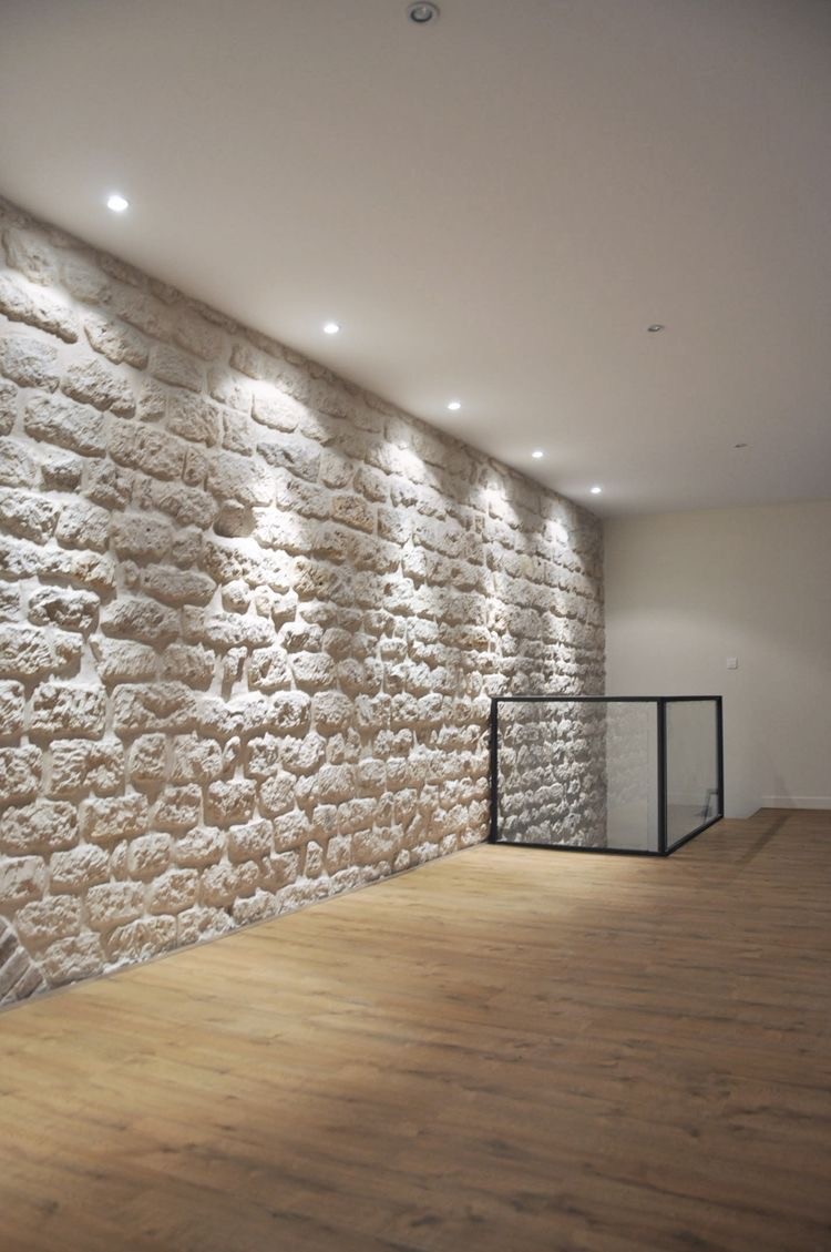 A modern hallway features vibrant teal and orange geometric and leaf patterns, with glossy tiled floors, a large rectangular light fixture, and a small shelf holding a potted plant, all leading to a large, frosted window at the end.