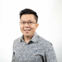 A smiling person wearing glasses and a patterned shirt stands against a plain white background.