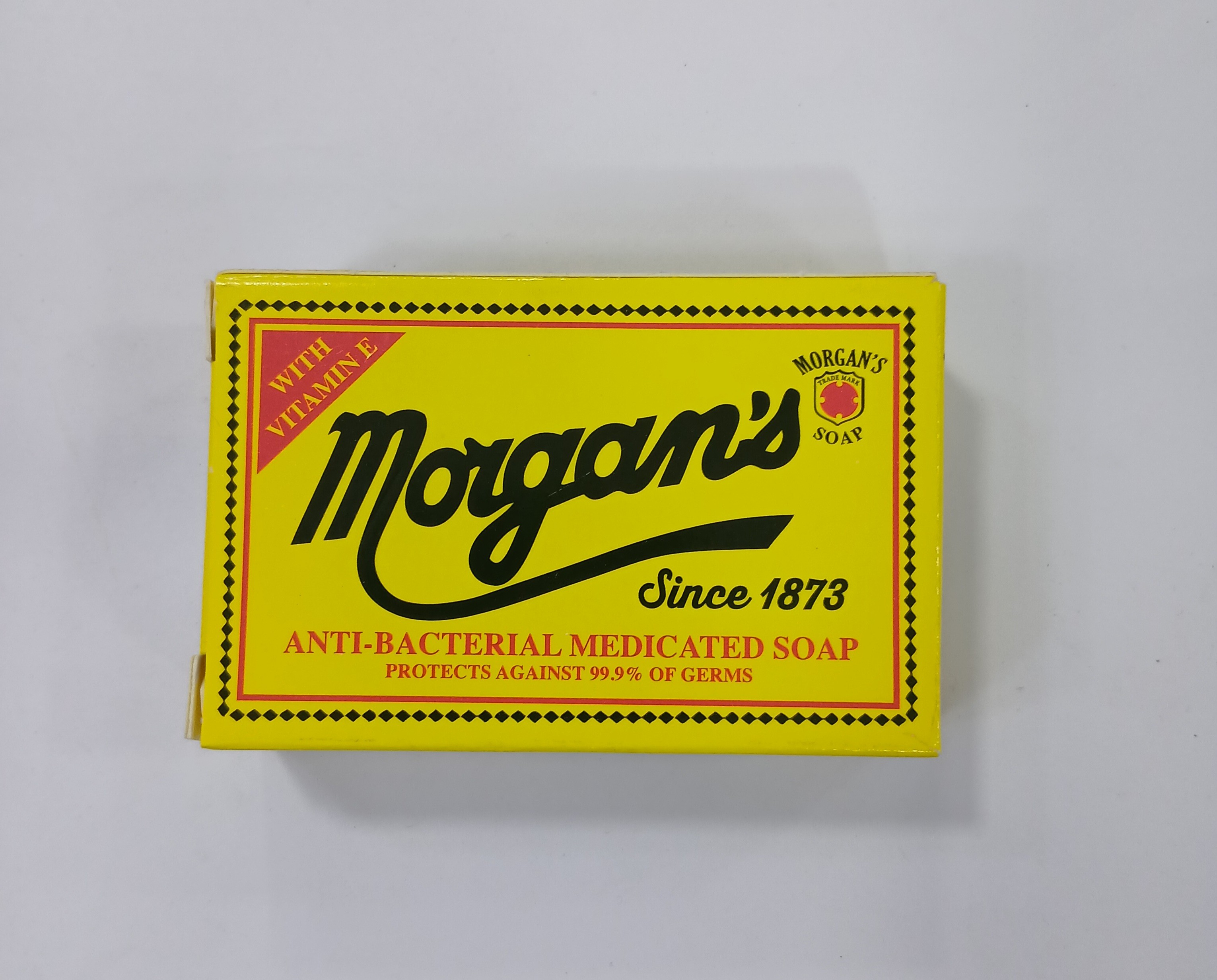 A yellow cardboard box with black and red text and decorative borders advertises anti-bacterial medicated soap protection against germs.