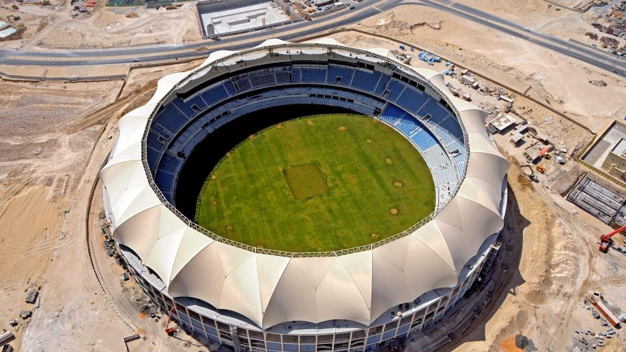 An aerial view of the Dubai International Stadium with a green field and blue seating areas under a white canopy. 