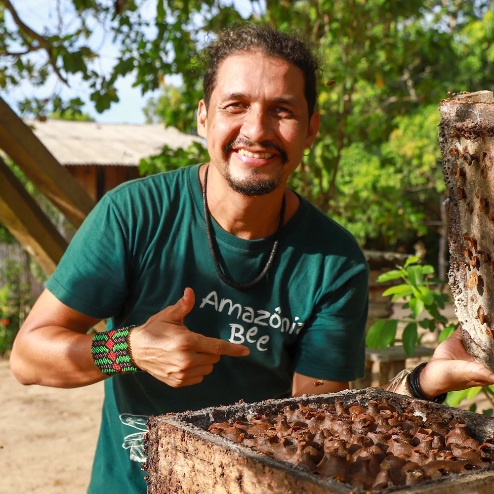 Homem meliponicultor sorrindo e apontando para uma melgueira.