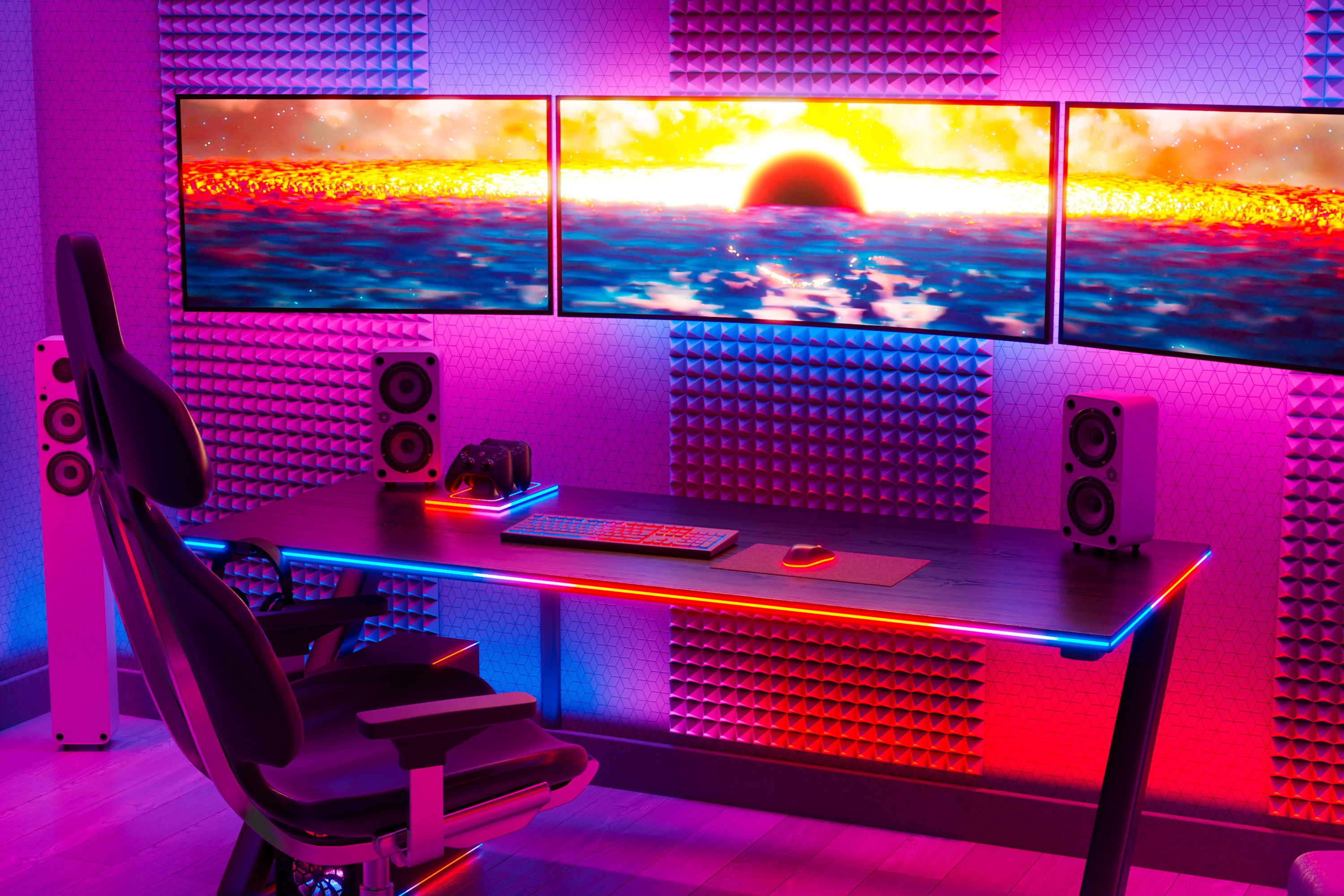 A gamer's room is illuminated by colorful lights. A computer chair, desk, speakers, monitors and few other electronics.