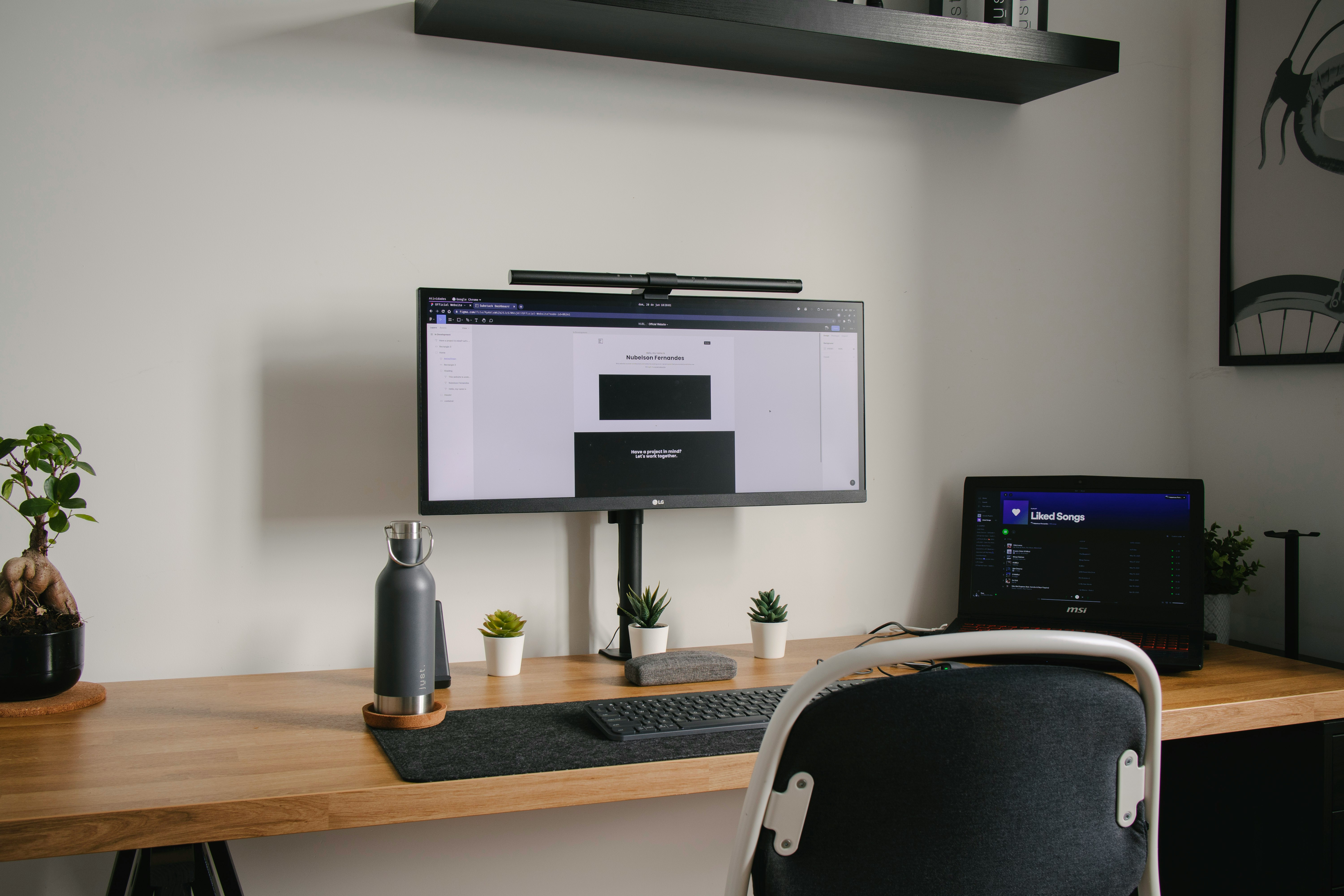 Minimal home office setup with a monitor, laptop, keyboard, desk accessories, and plants on a wooden desk.