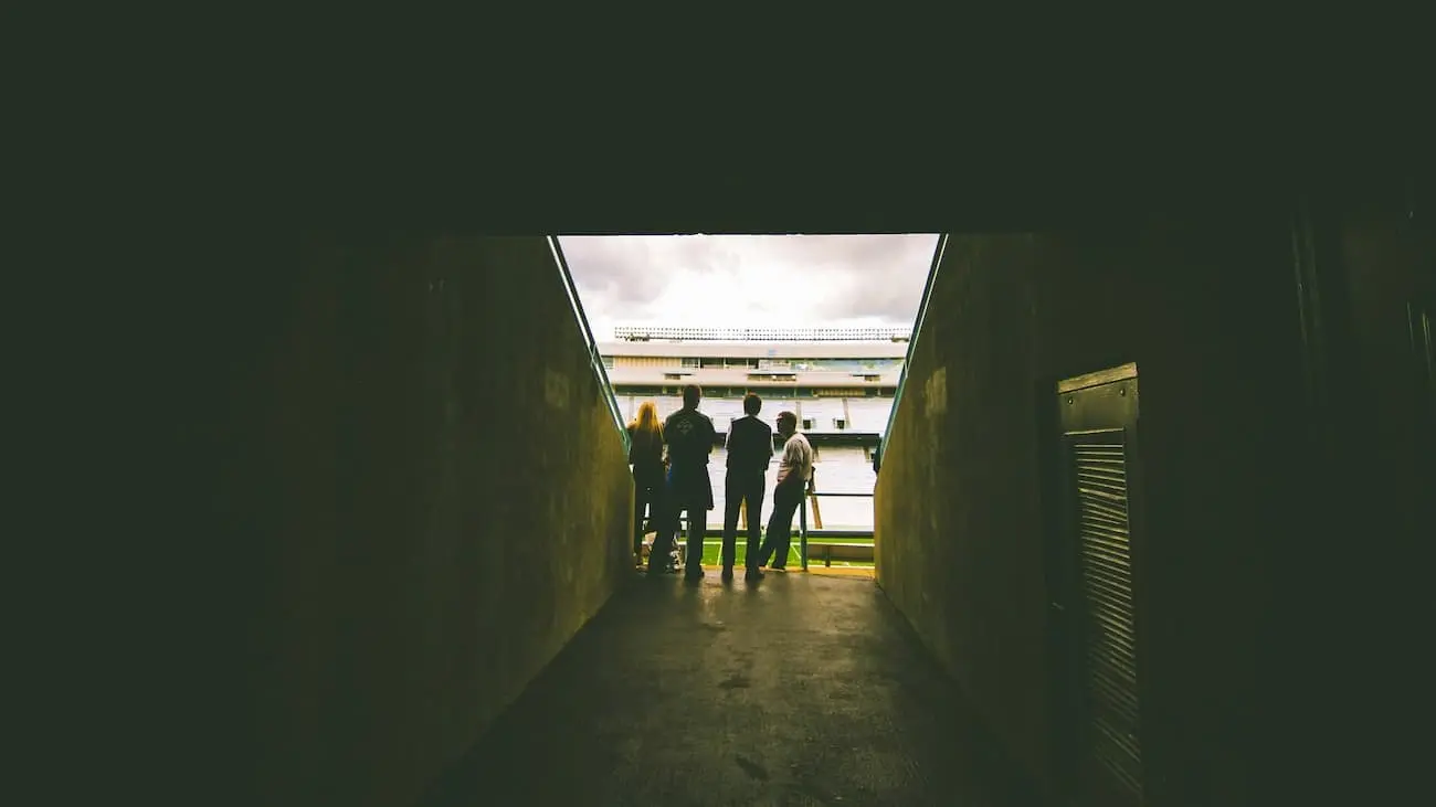 Four scouts stand at the end of a stadium tunnel and look out onto the pitch to scout players. The scene symbolises the view into the world of scouting in football, as discussed in the podcast episode on scouting in ambitious amateur football. The tunnel frame and the stadium behind it reinforce the feeling of expectation and analysis, in keeping with the theme of scouting.