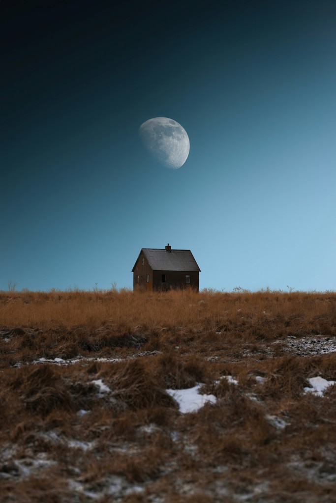 A small house in a field with the moon in the sky in the background