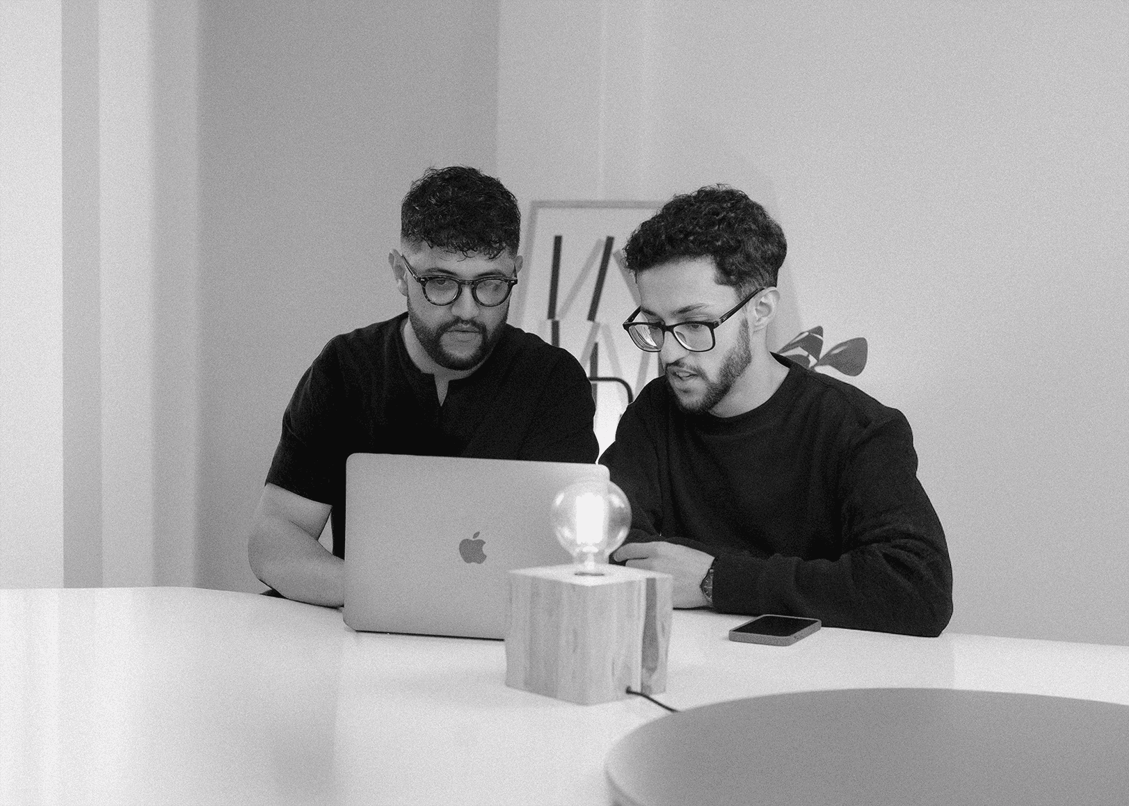 Black and white image of people working at a table with laptops, showing hands gesturing during discussion of digital content displayed on screens, with fabrica® logo in the corner.