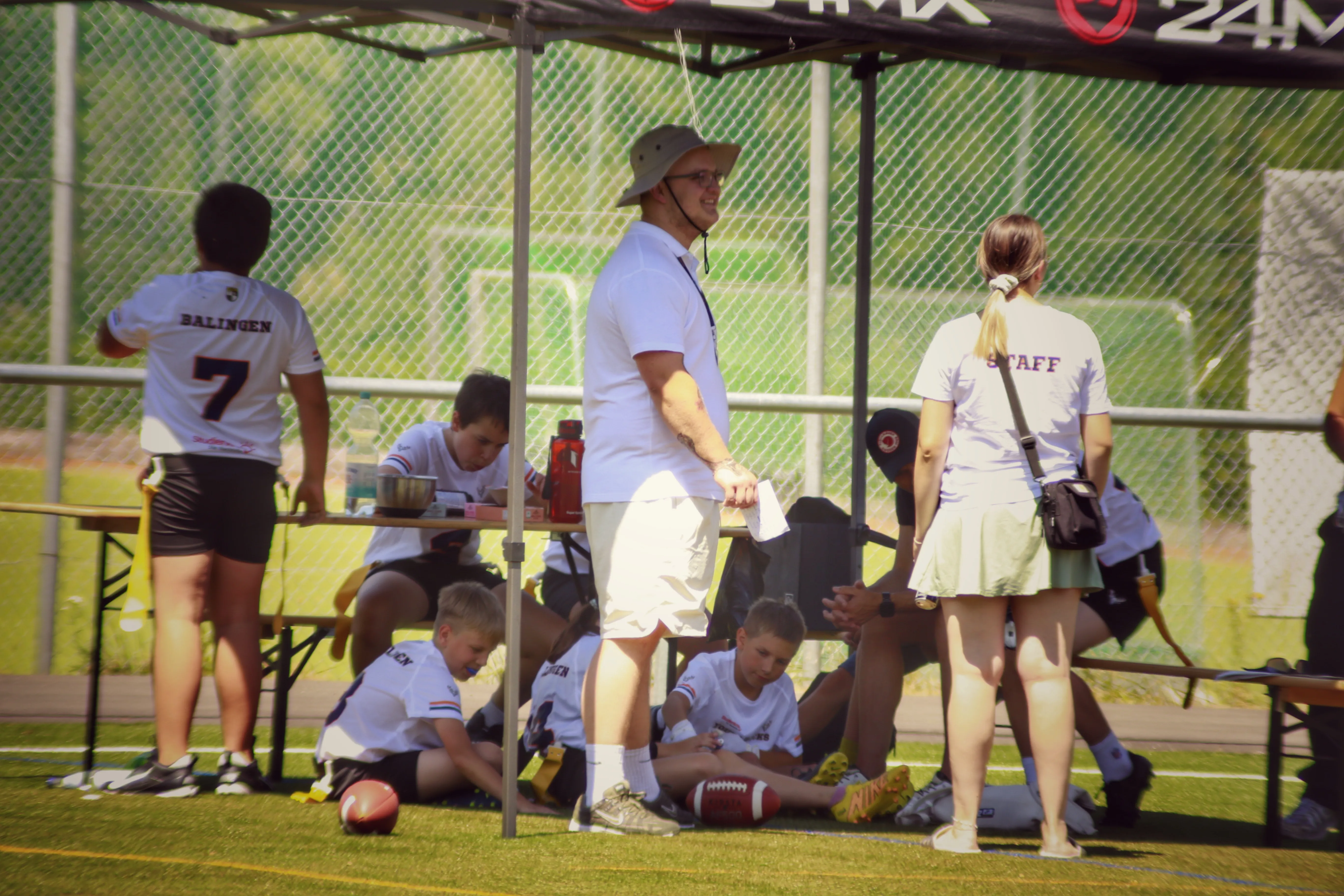 A group of athletes sitting on a bench while a coach stands nearby, discussing strategies during practice.