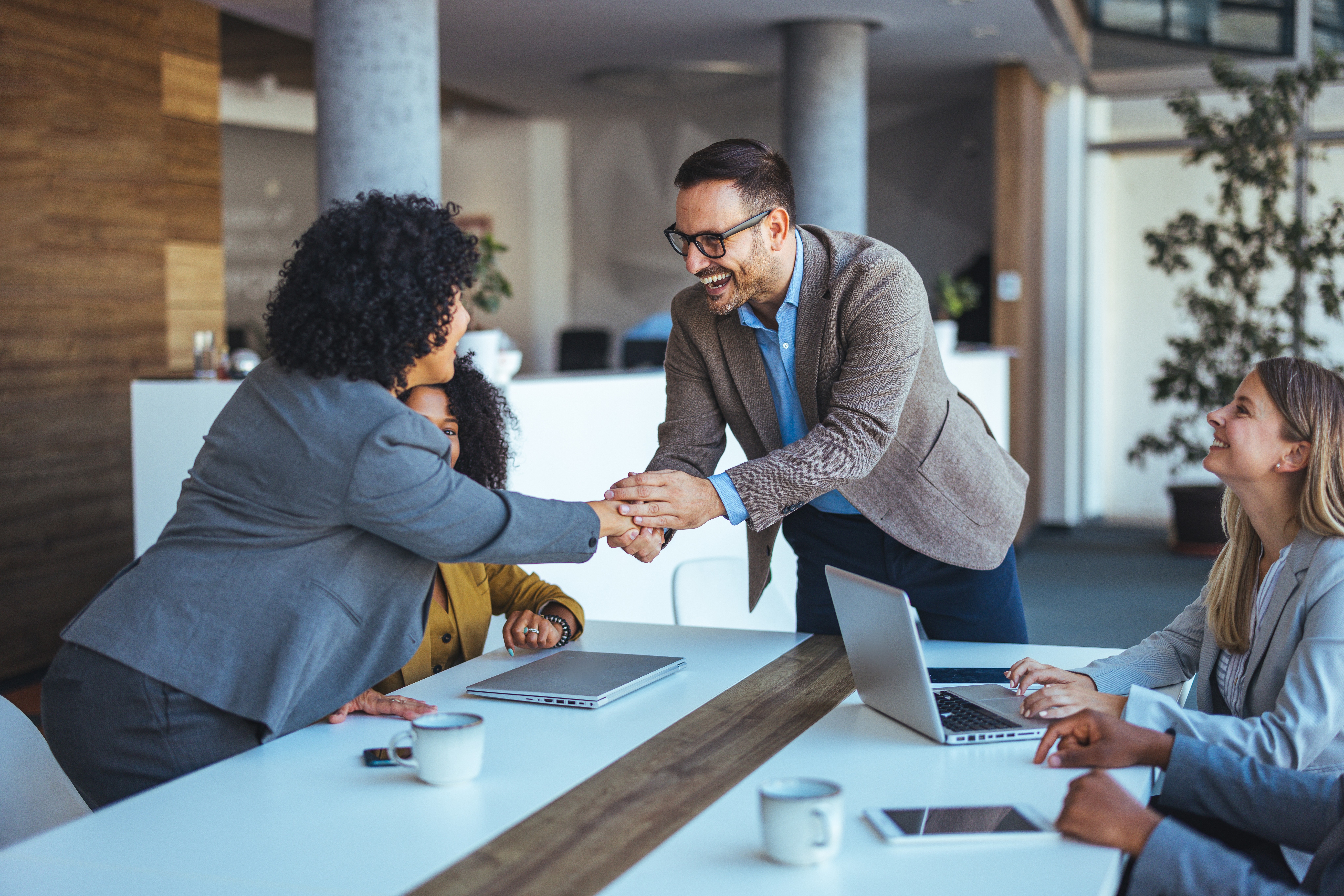 Older man in glasses sitting with laptop on coffee table, smiling while working.