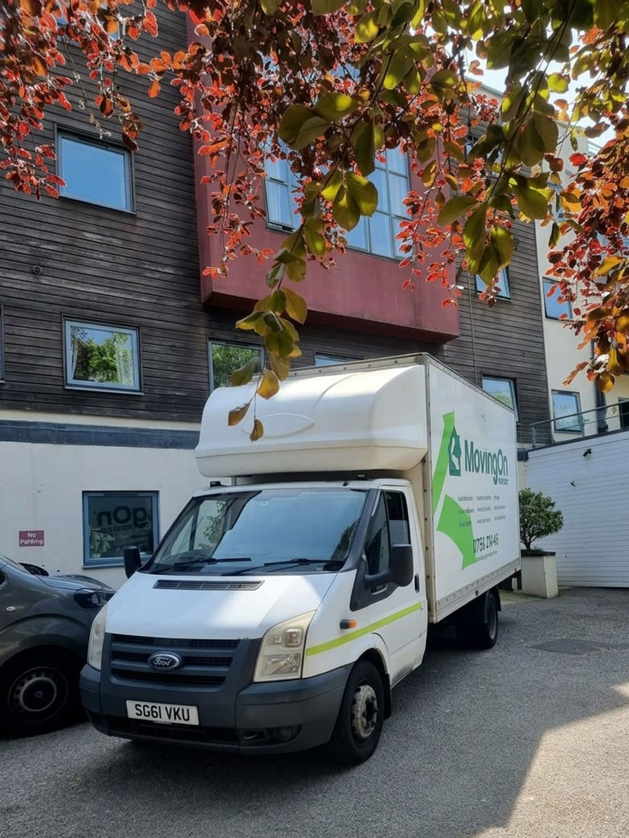 A Moving On Removals transit van parked outside a modern apartment building complex during a local house-to-retirement-home relocation in Plympton.