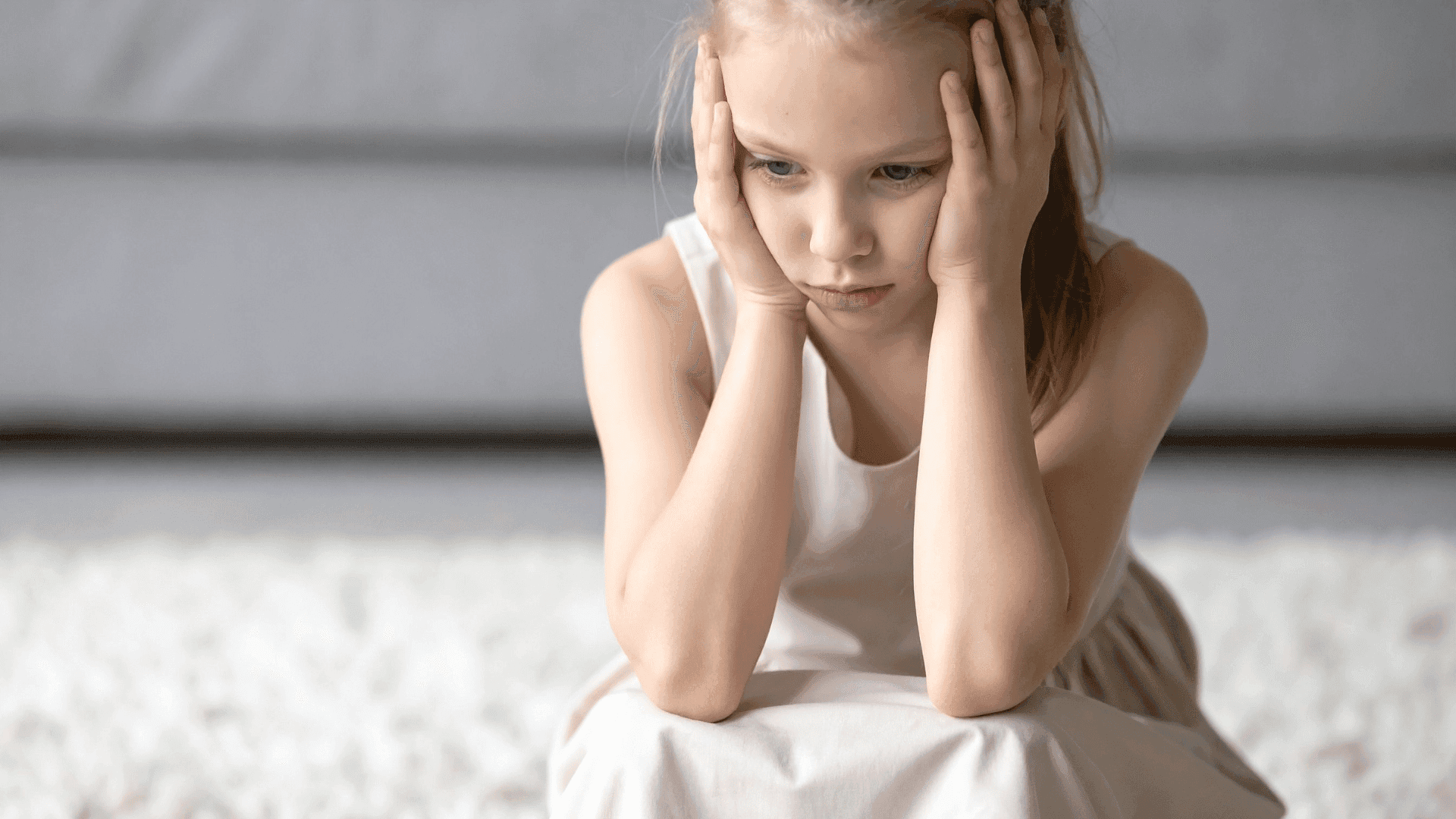A young girl sitting alone, looking upset and stressed.