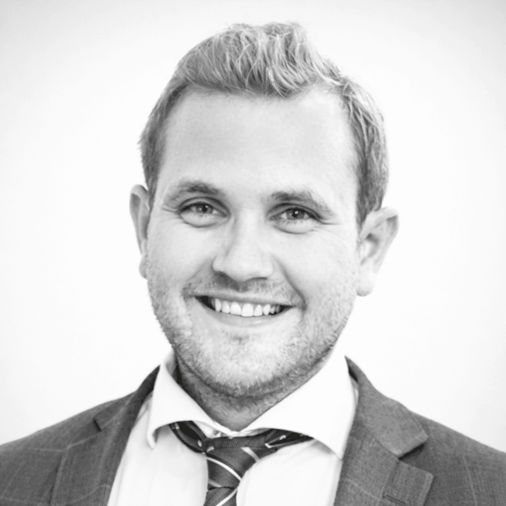 A person with medium-length brown hair wearing a dark, textured coat and a burgundy turtleneck. They have a calm, neutral expression.