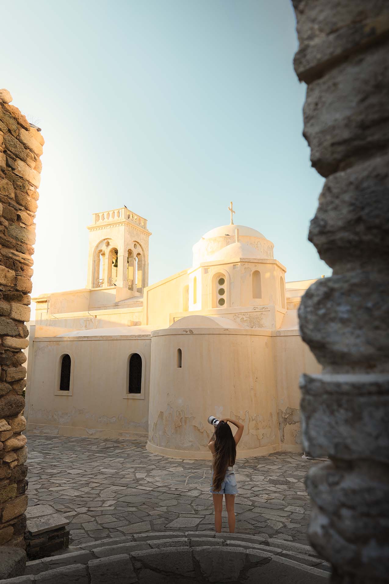 Girl taking a photo of a church building at sunset with sunlight hitting it.