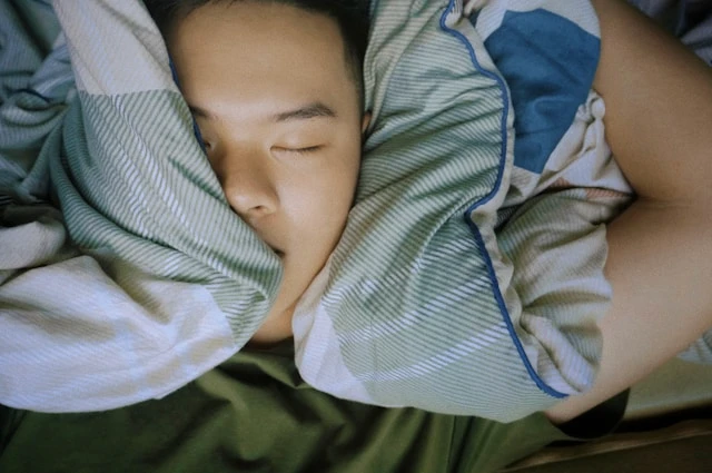Person sleeping peacefully with their face partly covered by a blanket