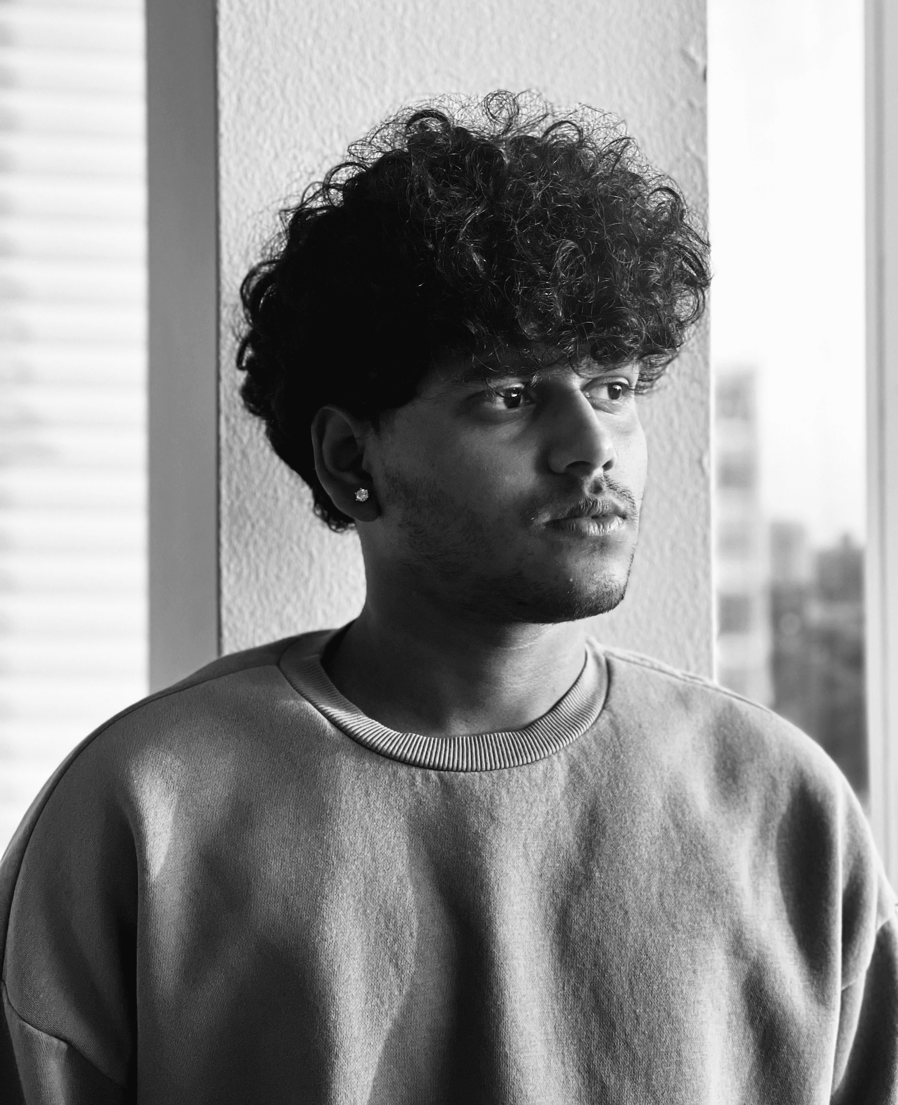 Close-up portrait of a person wearing a gray insulated hooded jacket with the hood up, showing their face framed by the hood against a light background.