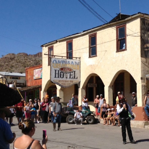 人们聚集在历史悠久的西式小镇的奥特曼酒店外面，背景是沙漠丘陵。