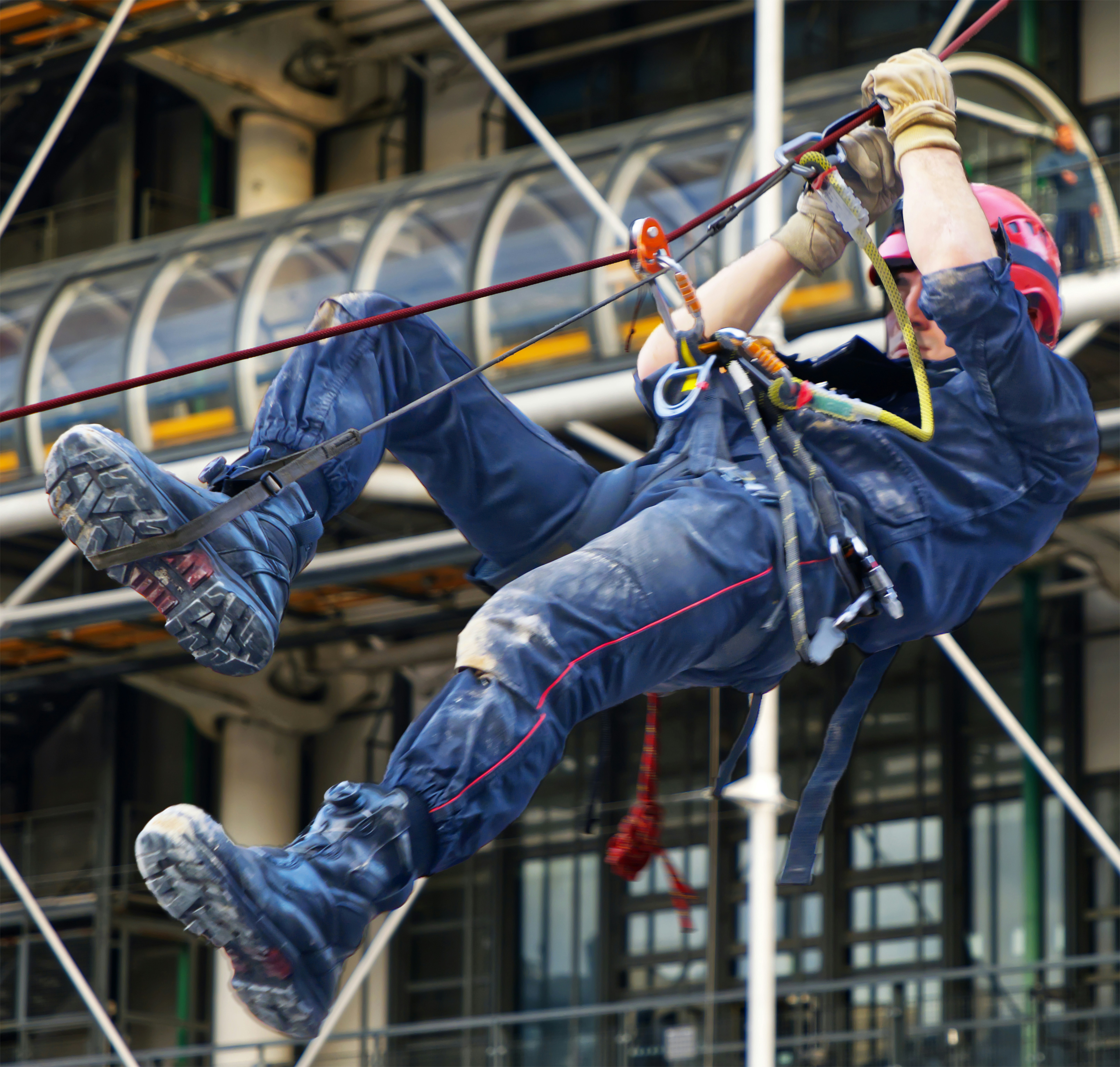 A construction worker rappelling down a building, wearing safety gear and using ropes for support.