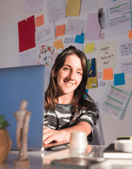 Young woman typing on her laptop and smiling at the camera in a workspace