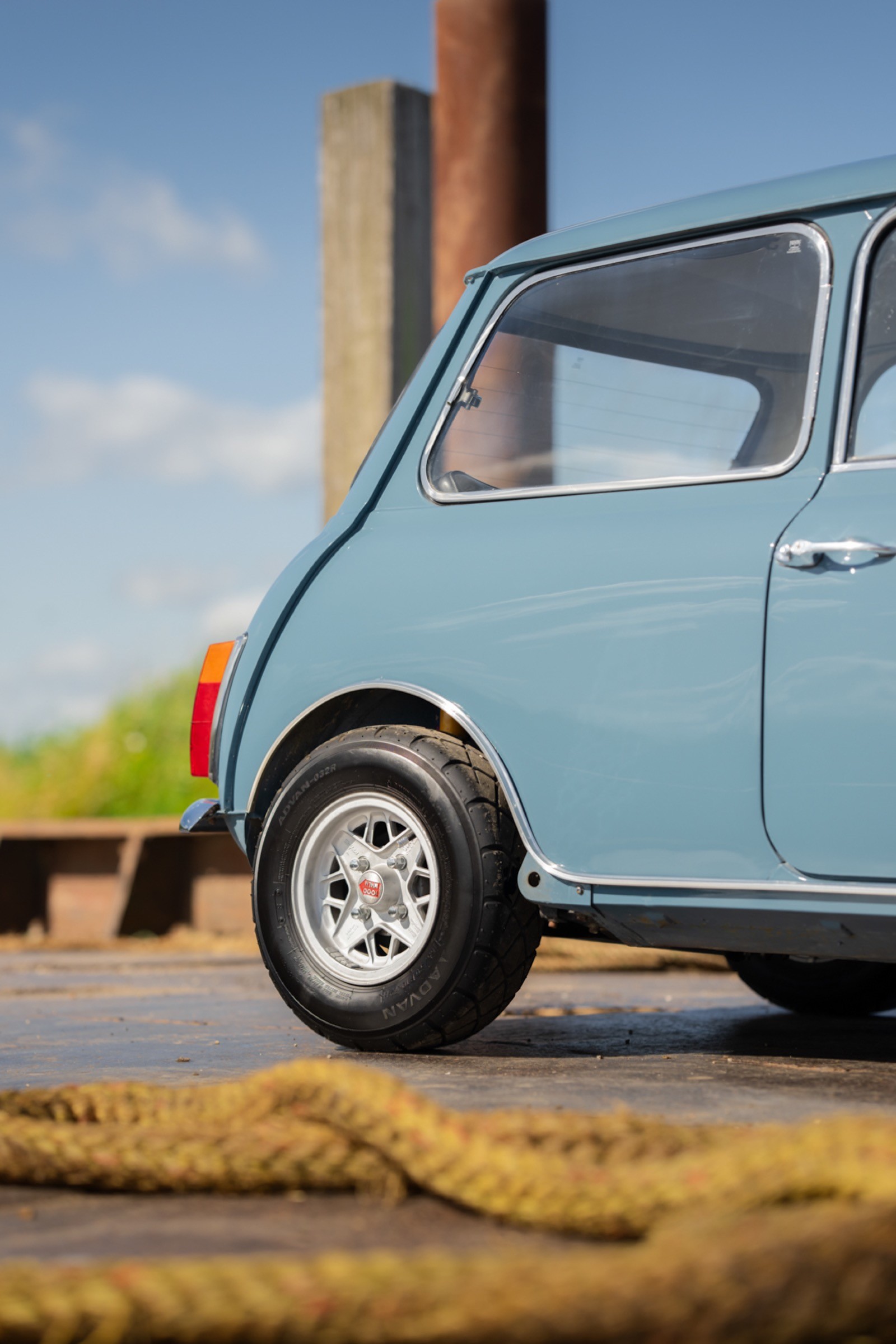 A close-up of a vintage blue car with a shiny wheel, set against a sunny, outdoor background.