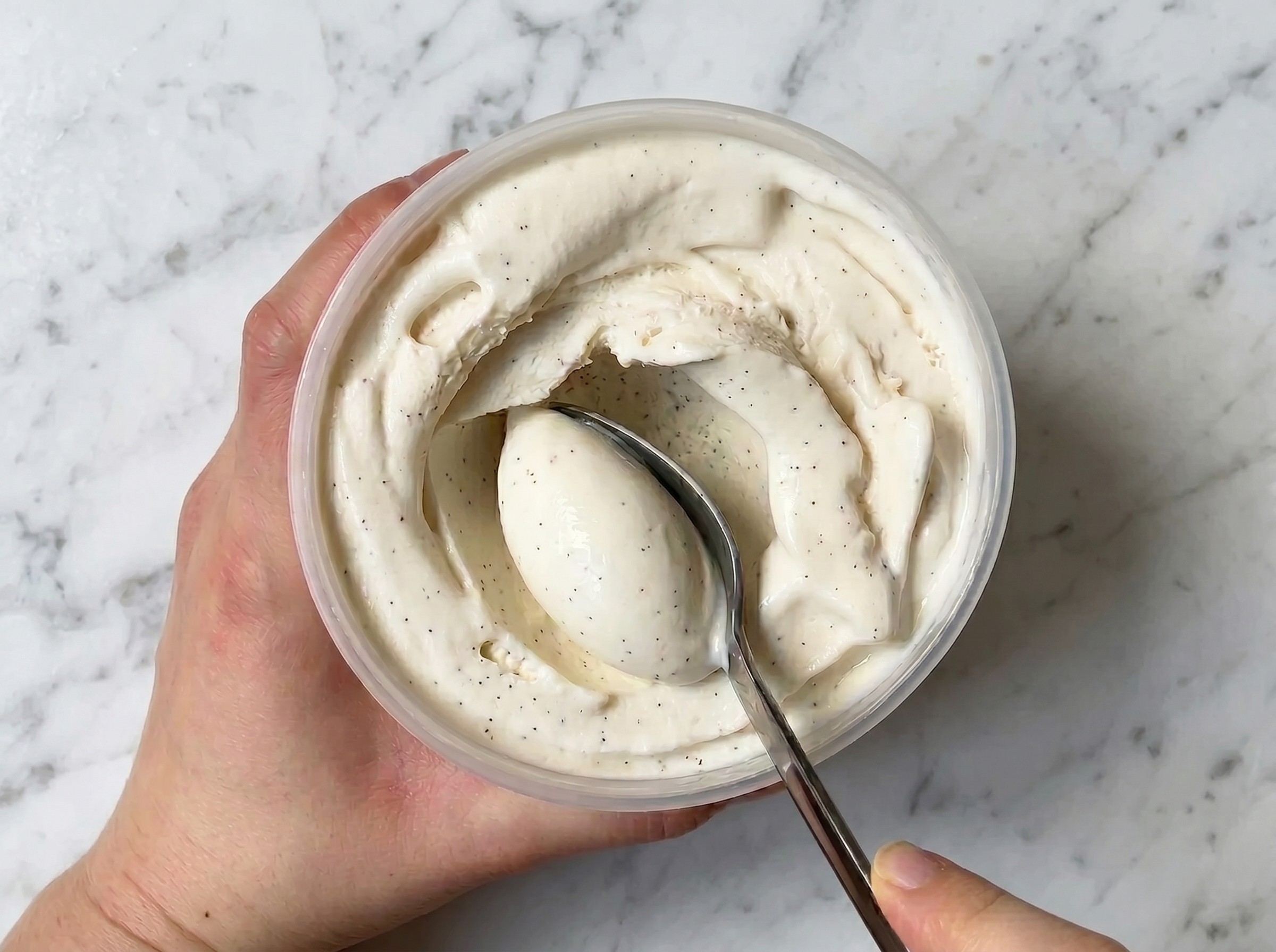 Hand holding a container of vanilla ice cream with a spoon.