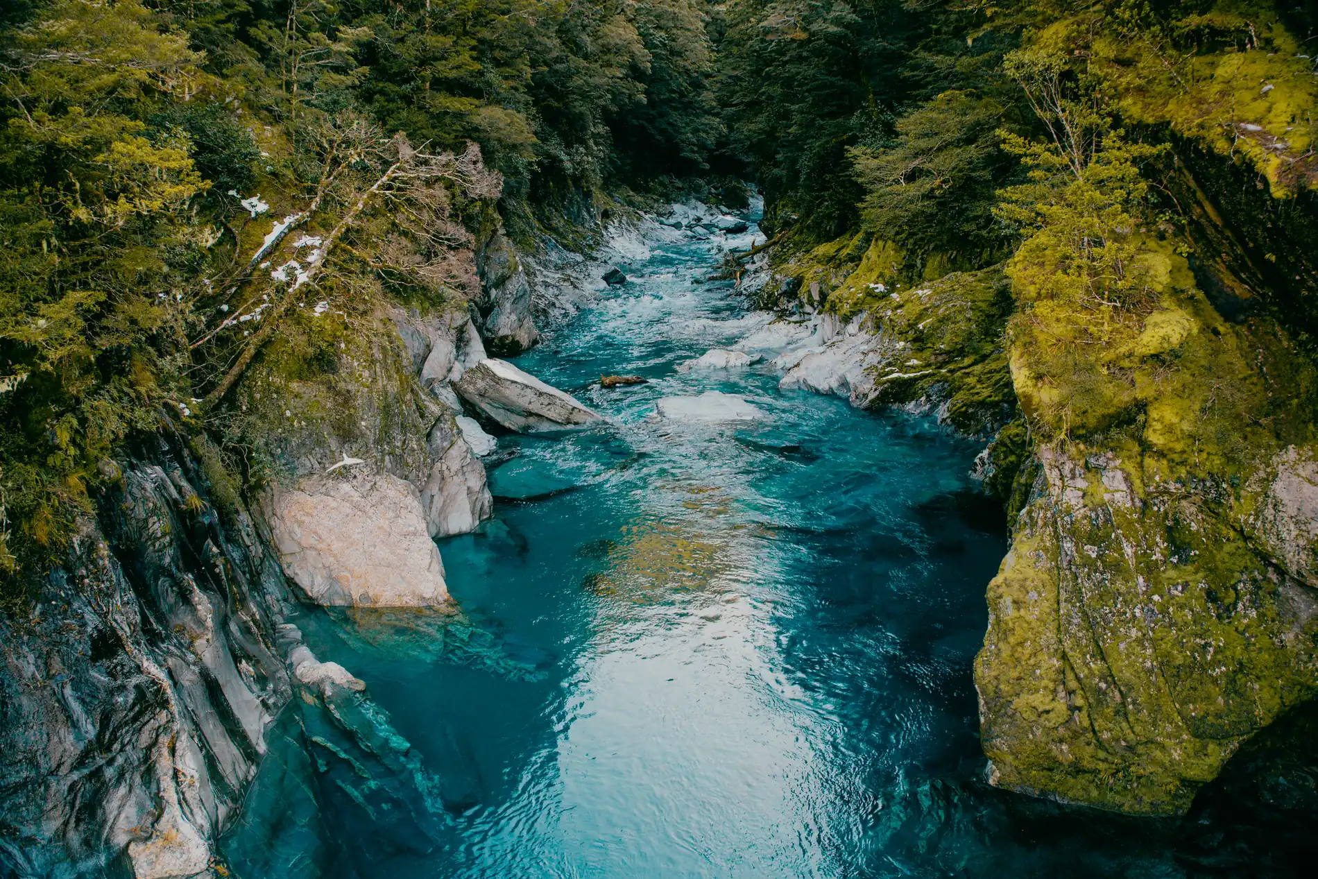 Aerial of a turquoise river pooling between mossy rock walls in dense forest