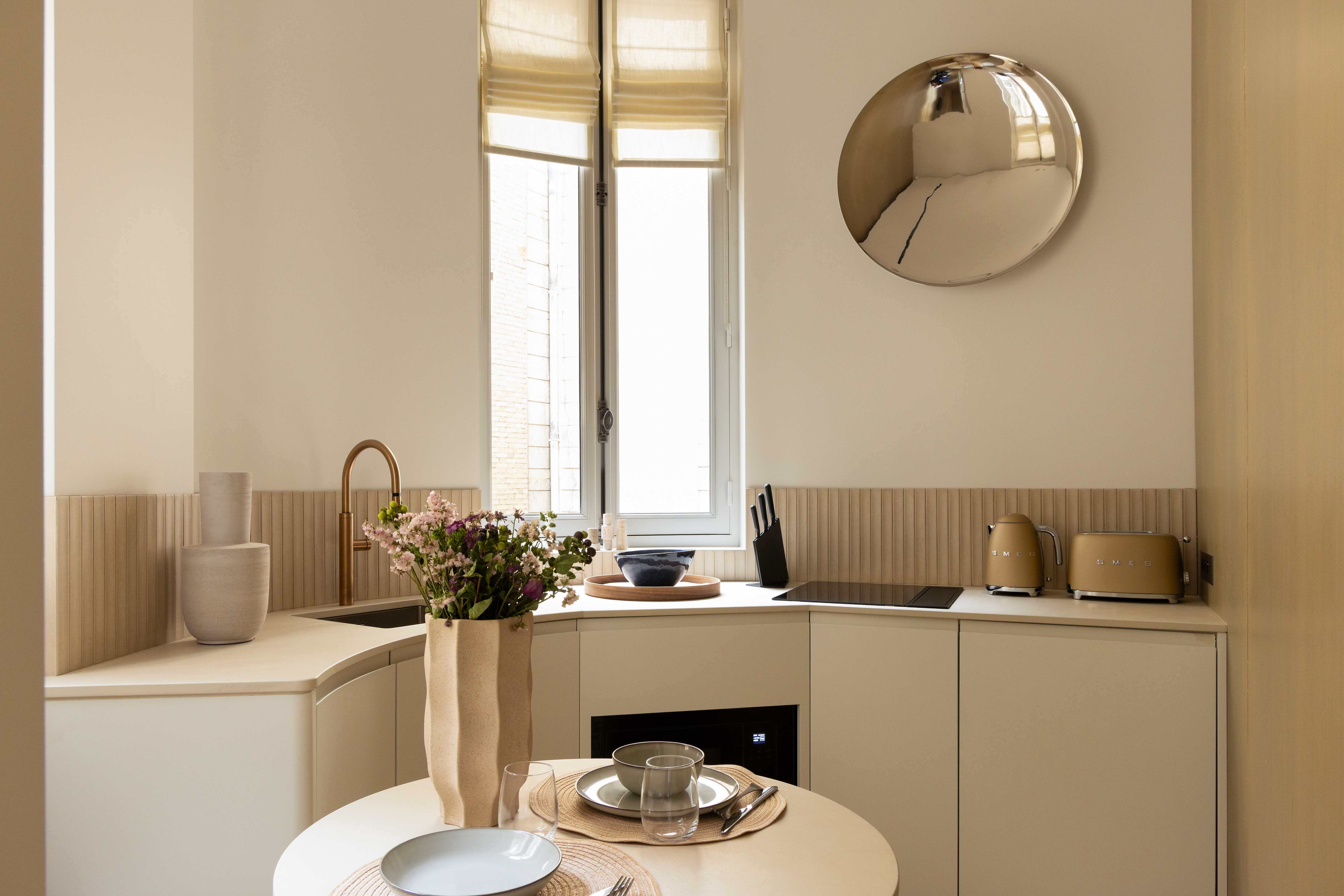 Kitchenette avec robinetterie doree, credence cannelee beige, miroir convexe chrome, bouquet et appareils Smeg dores