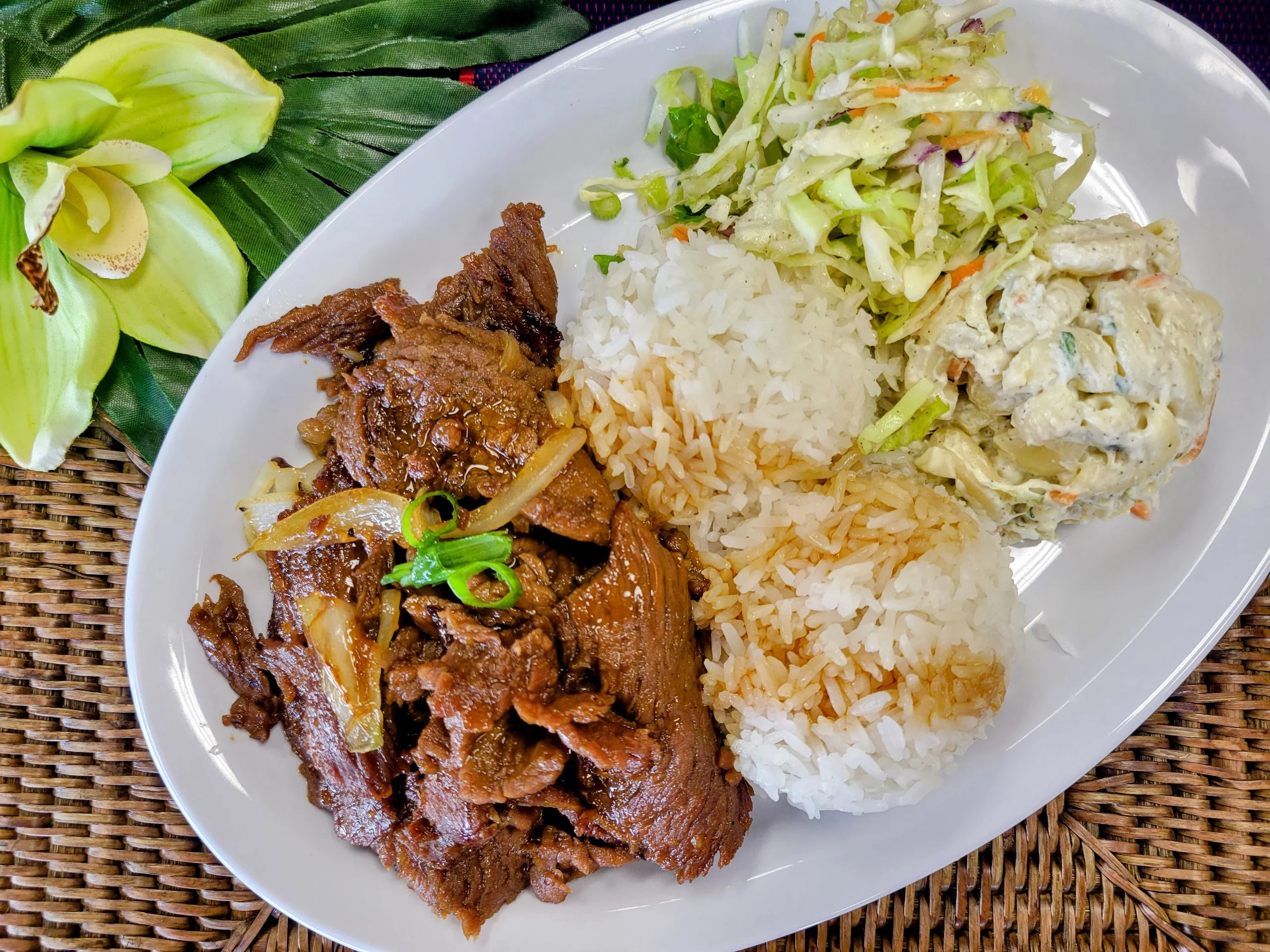 Thinly sliced Hawaiian Grilled Beef topped with green onions, served with two scoops of rice and traditional sides in a bowl.
