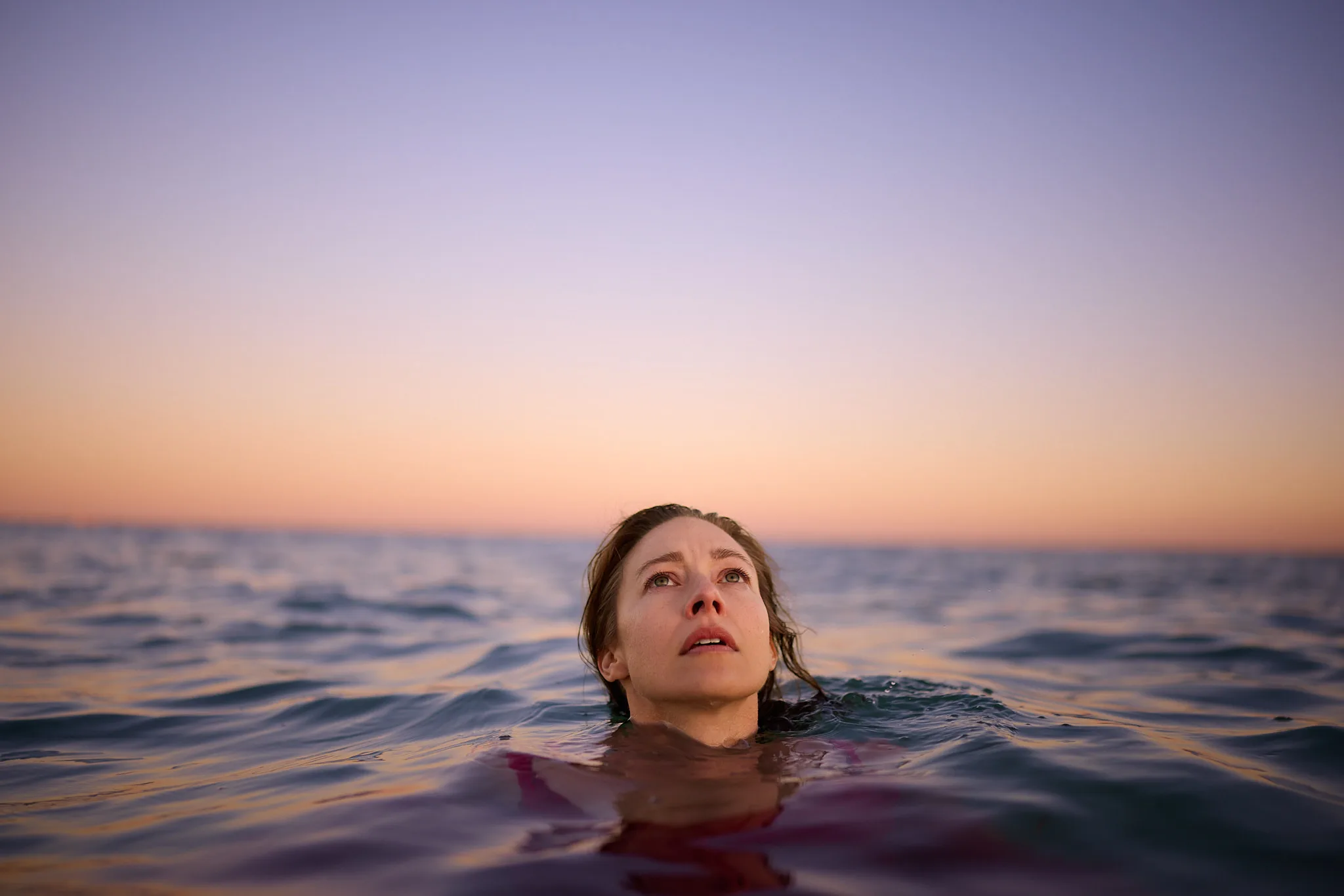 woman surfacing in open water at dusk — portrait photography by Tom Kubik