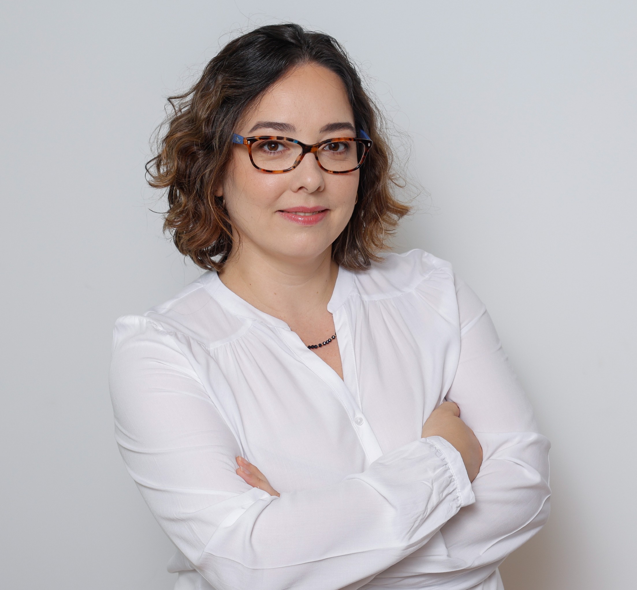 Smiling female therapist with short gray hair, wearing a brown top and a purple shawl, surrounded by a cozy background.
