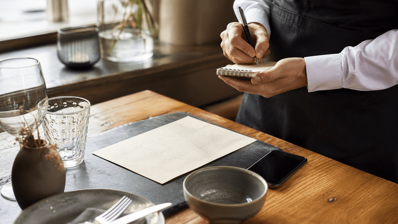 Table de restaurant avec ardoise, smartphone éteint et serveur, évoquant le prix d’un site.