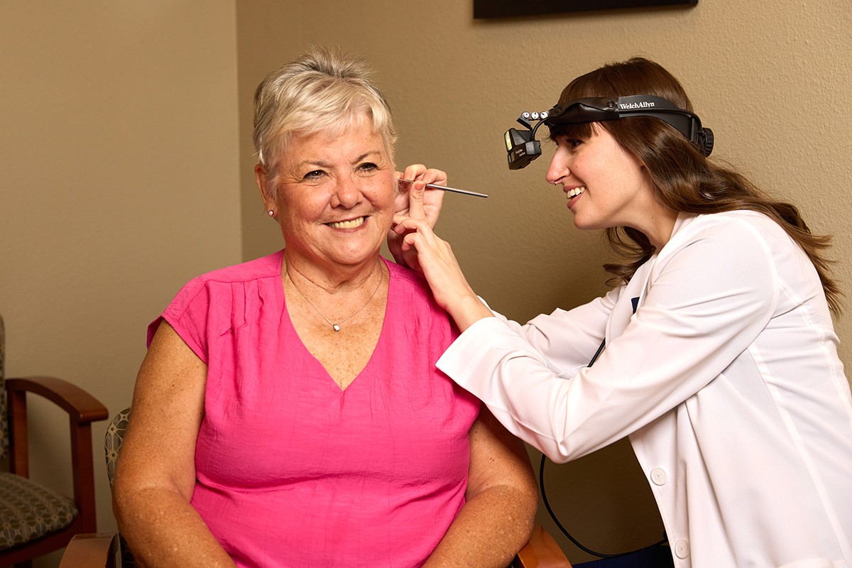 A woman smiles as another applies makeup to her cheek, showcasing a warm and lively interaction.