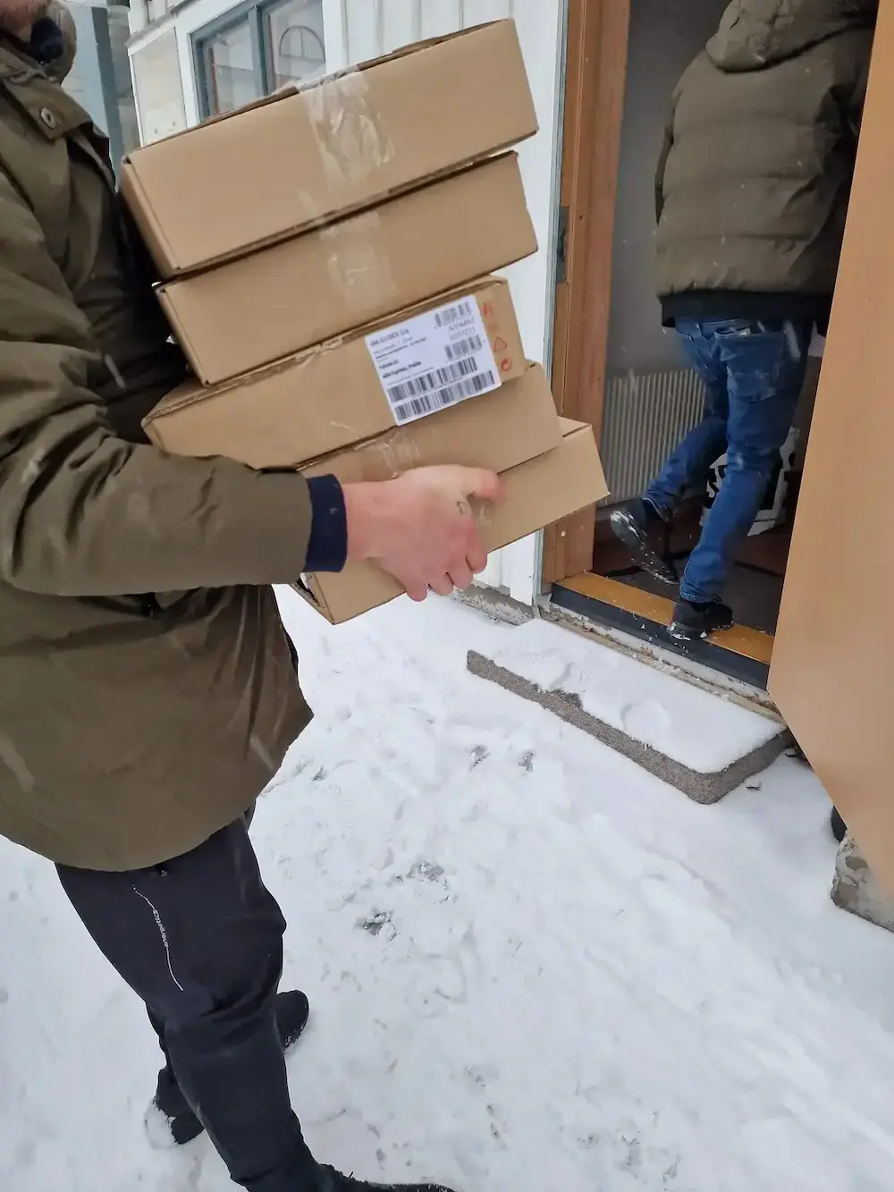 Person bär flera kartonger med levererade donationer in i Vinternatts lokaler under vintertid.