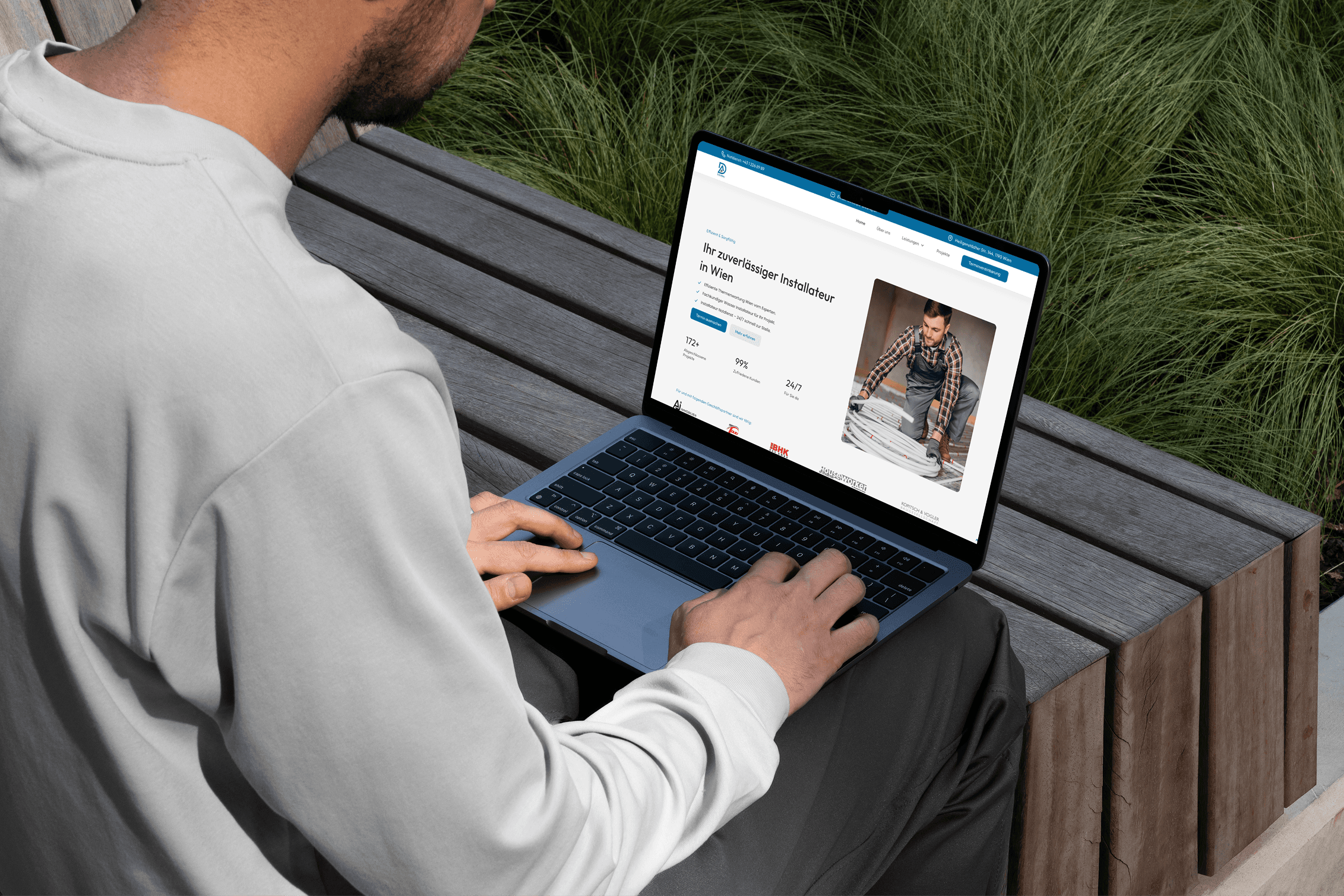 A woman in an orange sweater, wearing glasses, focused on coding at a computer screen.