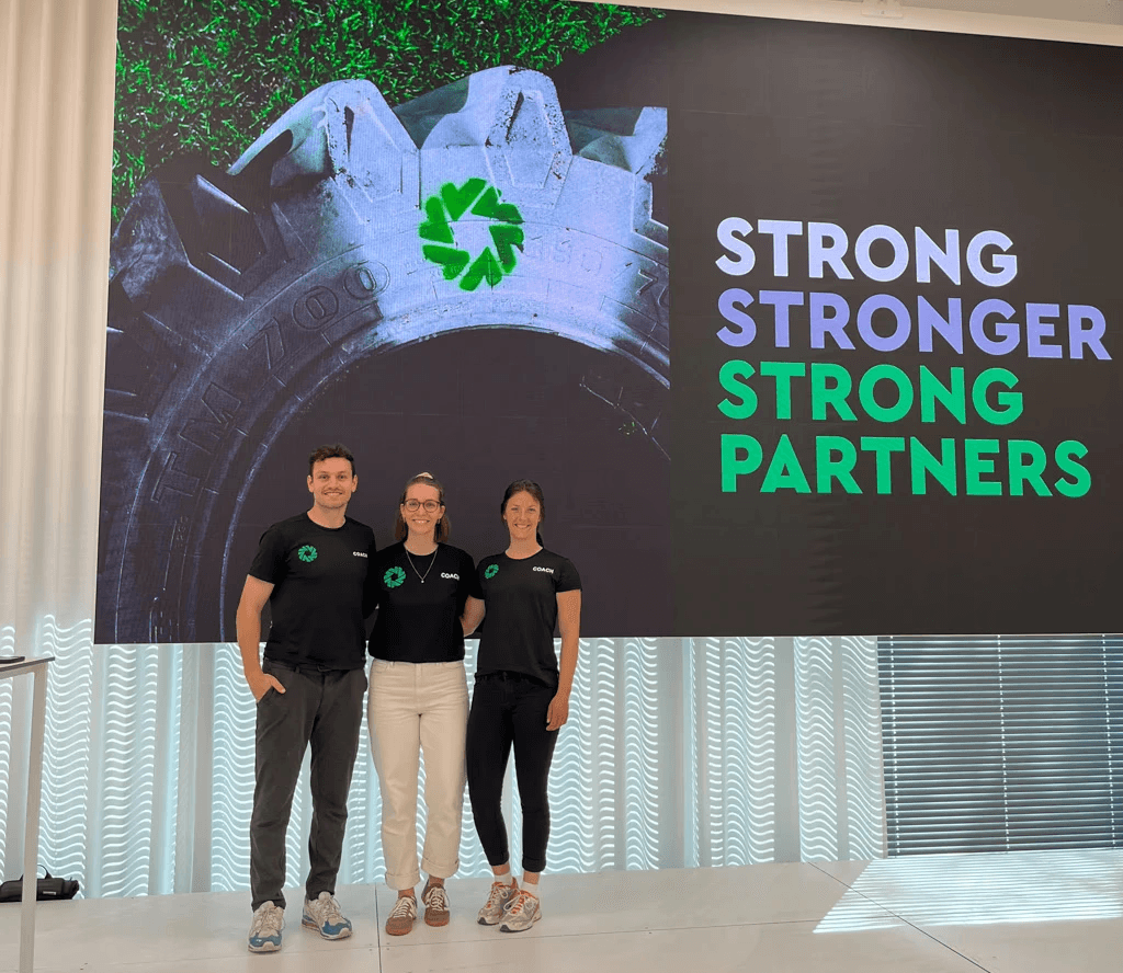 Ein junger Mann steht neben zwei jungen Frauen, alle drei haben Strong Partners Shirts an. Sie stehen vor einer Präsentation mit dem Titel Strong, Stronger, Strong Partners