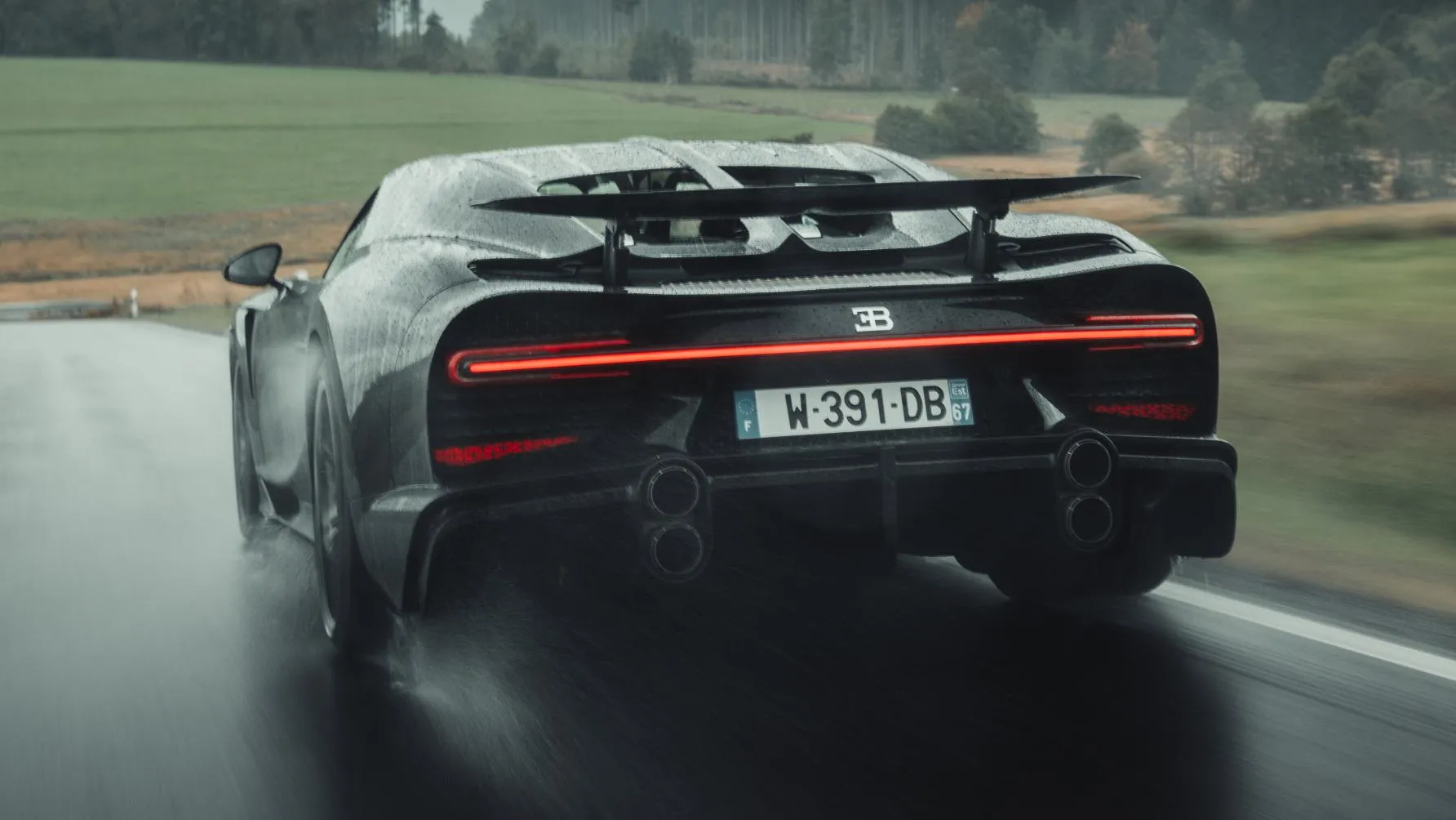 Rear view of a black hypercar driving on a wet road