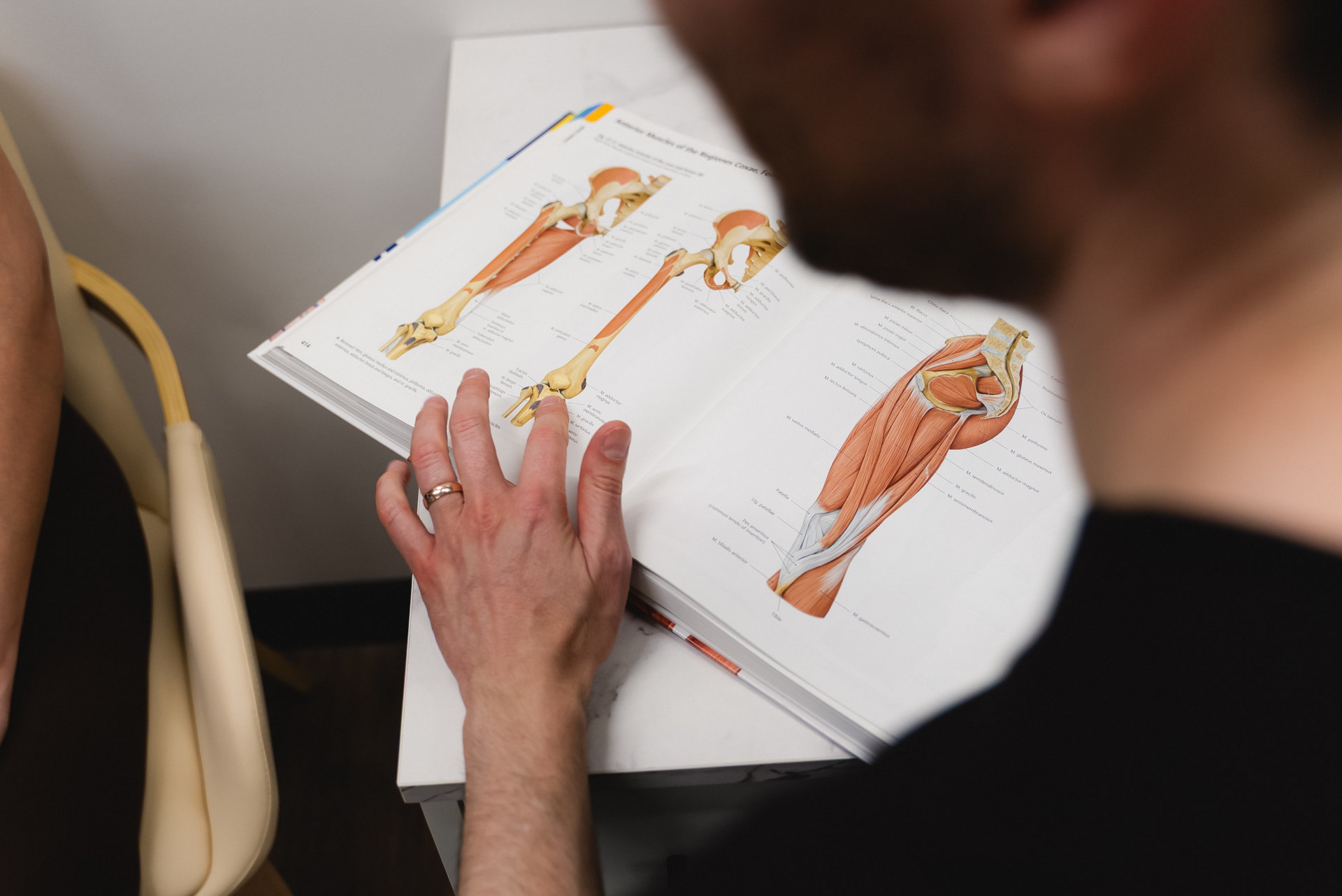 A closeup of an anatomy textbook with a male hand pointing to a drawing of a knee joint