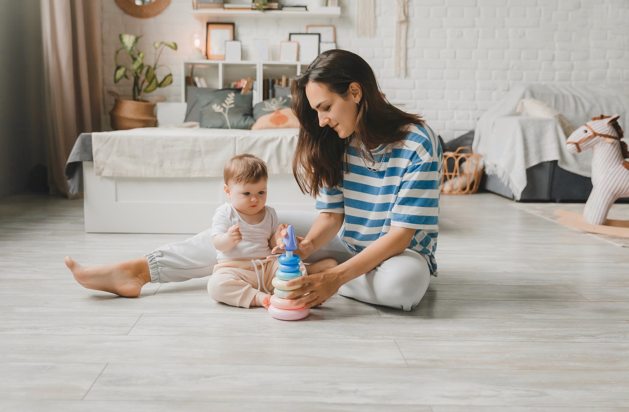 A mother and baby playing together on light wood-look flooring in a cozy bedroom, showcasing LUXO Floors’ durable and family-friendly surface ideal for homes with children.
