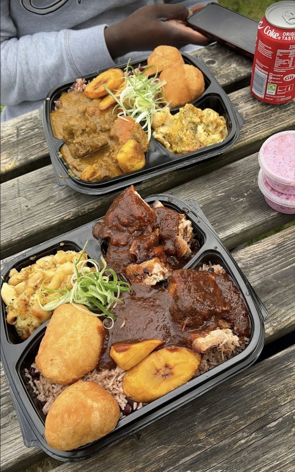 A takeaway meal with rice, plantain and dumplings on a wooden picnic table