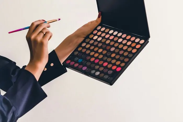 A person holding a large multi-shade eyeshadow palette and a brush