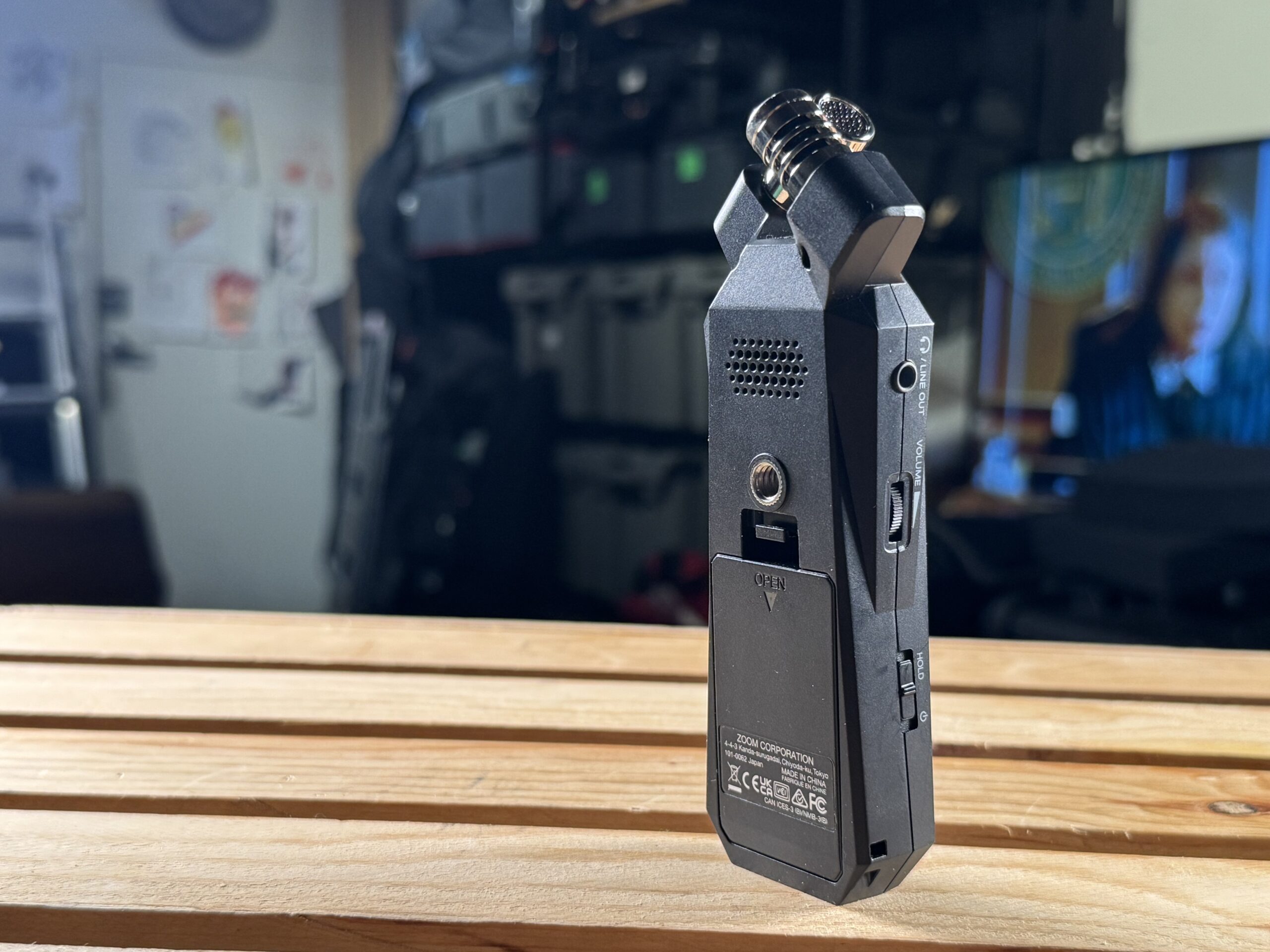 Rear view of a Zoom portable audio recorder on a wooden surface, showing the battery door and speaker.