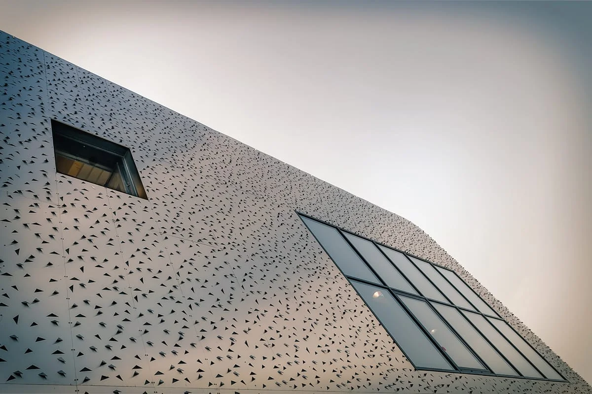 Façade perforée blanche avec fenêtre triangulaire en contre plongée — architecture contemporaine à seclin