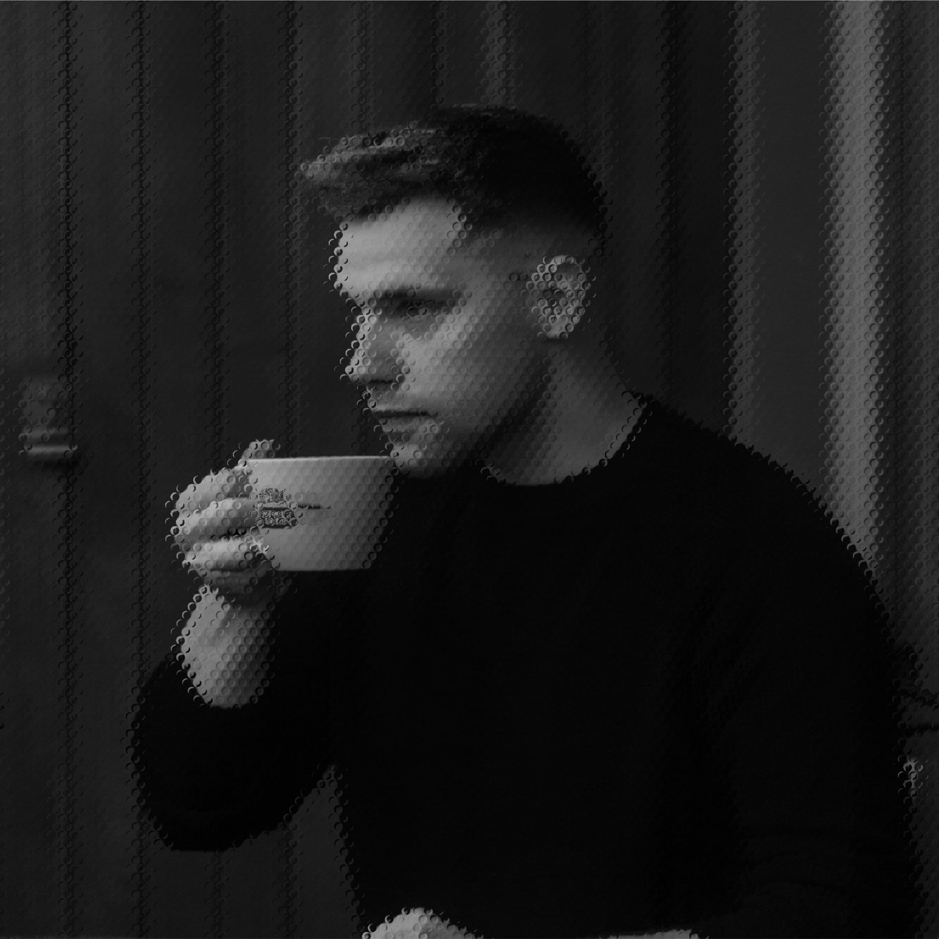 A person in a dimly lit room is holding a white mug near their face, appearing thoughtful, with vertical wooden panels in the background.