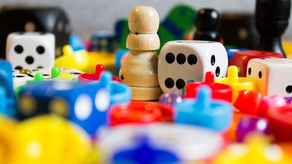 A close-up of colourful board game pieces including wooden pawns, plastic tokens and dice scattered together.
