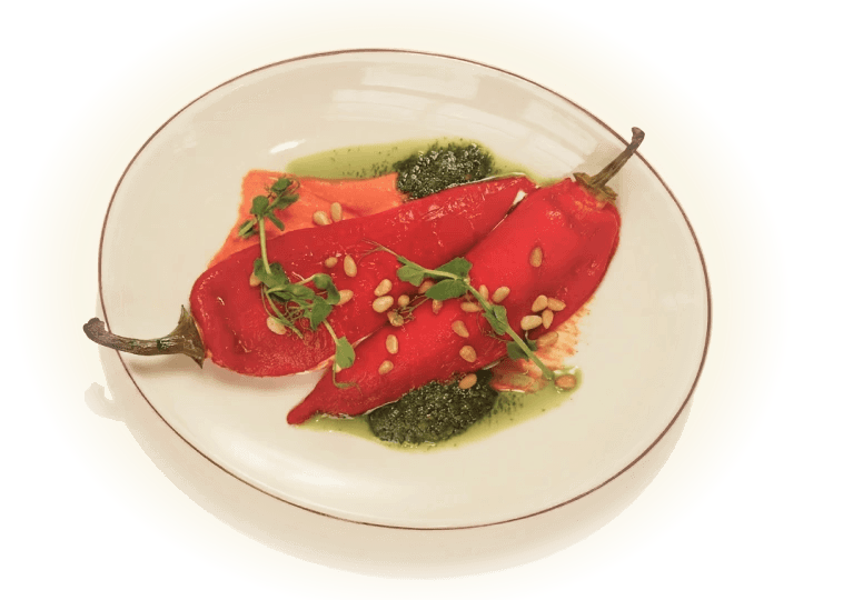 Roasted red peppers on a white plate with pesto, pine nuts, and microgreens.