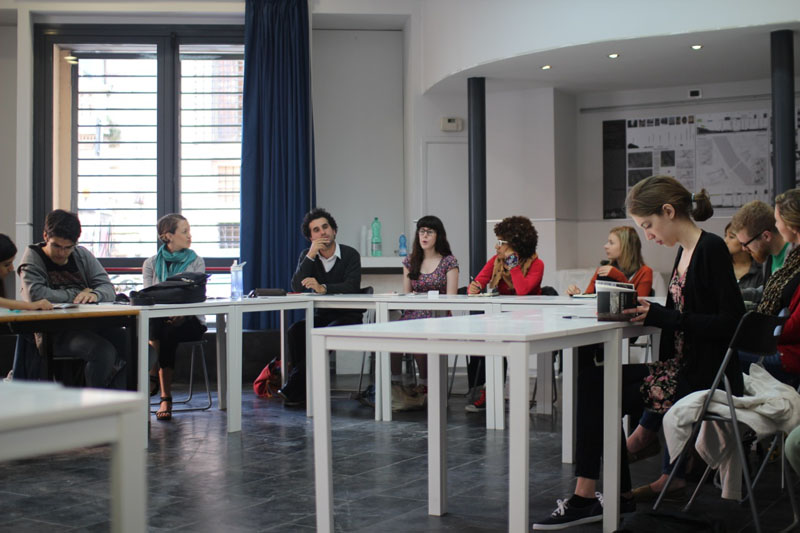 A photo of several students sitting at tables and following a lecture.