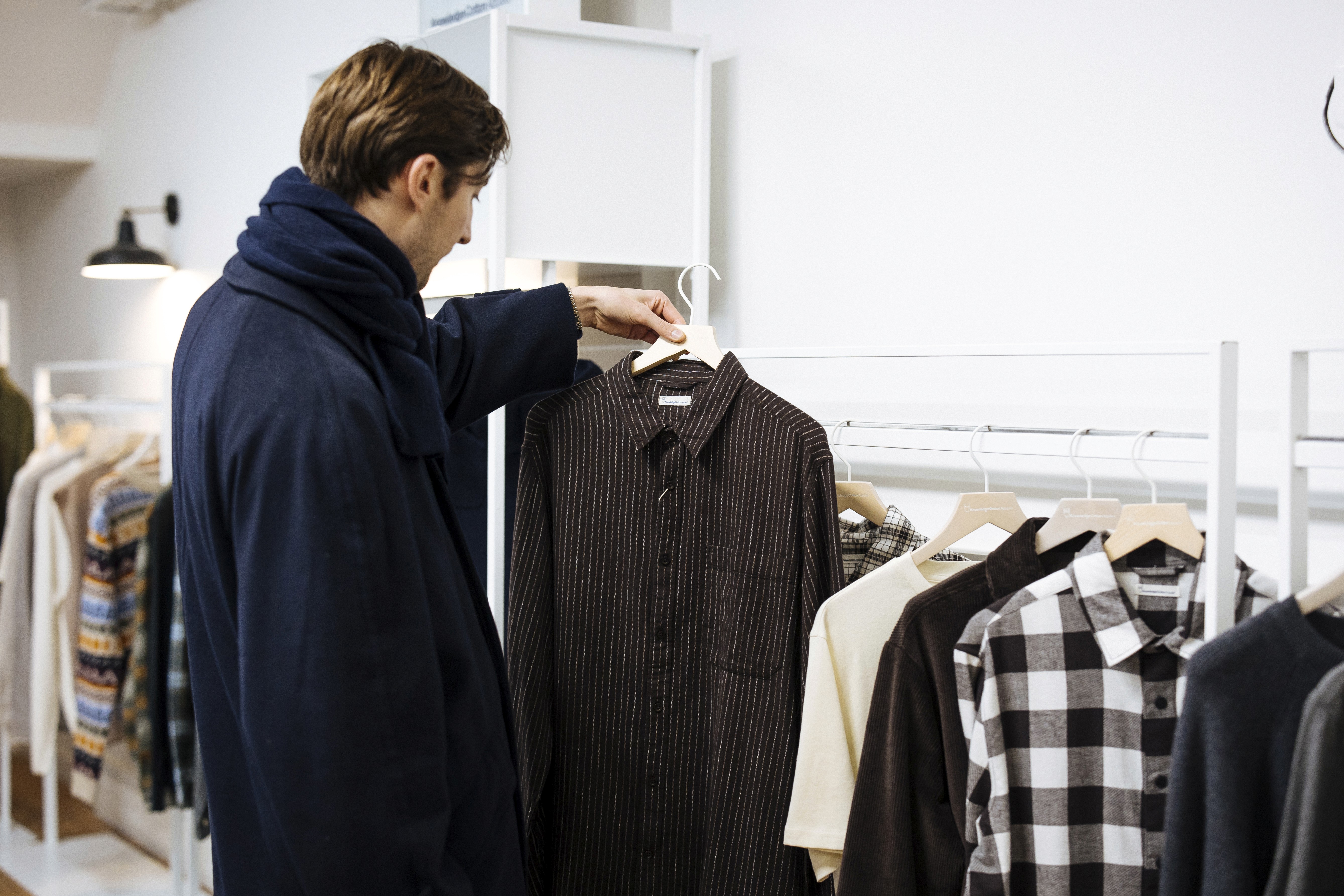 Client parcourant la sélection de chemises KnowledgeCotton Apparel dans le showroom Clothette à Paris.
