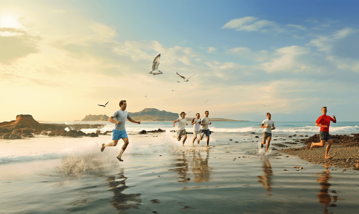 Group of people running on a sunny beach, splashing in the waves.