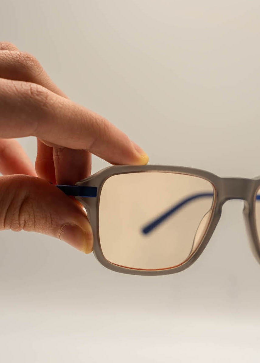 Athletic man in a sleeveless black outfit posing confidently outdoors under a bright blue sky, with a close-up of navy and salmon-colored men’s running shoes in the foreground.