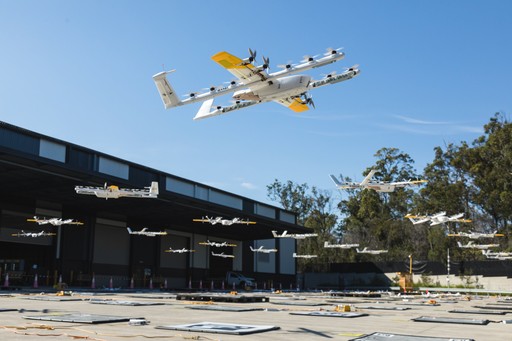 A fleet of delivery drones hovers above a tech company's distribution center, set against a clear blue sky and surrounded by lush trees, showcasing innovative logistics and drone technology.